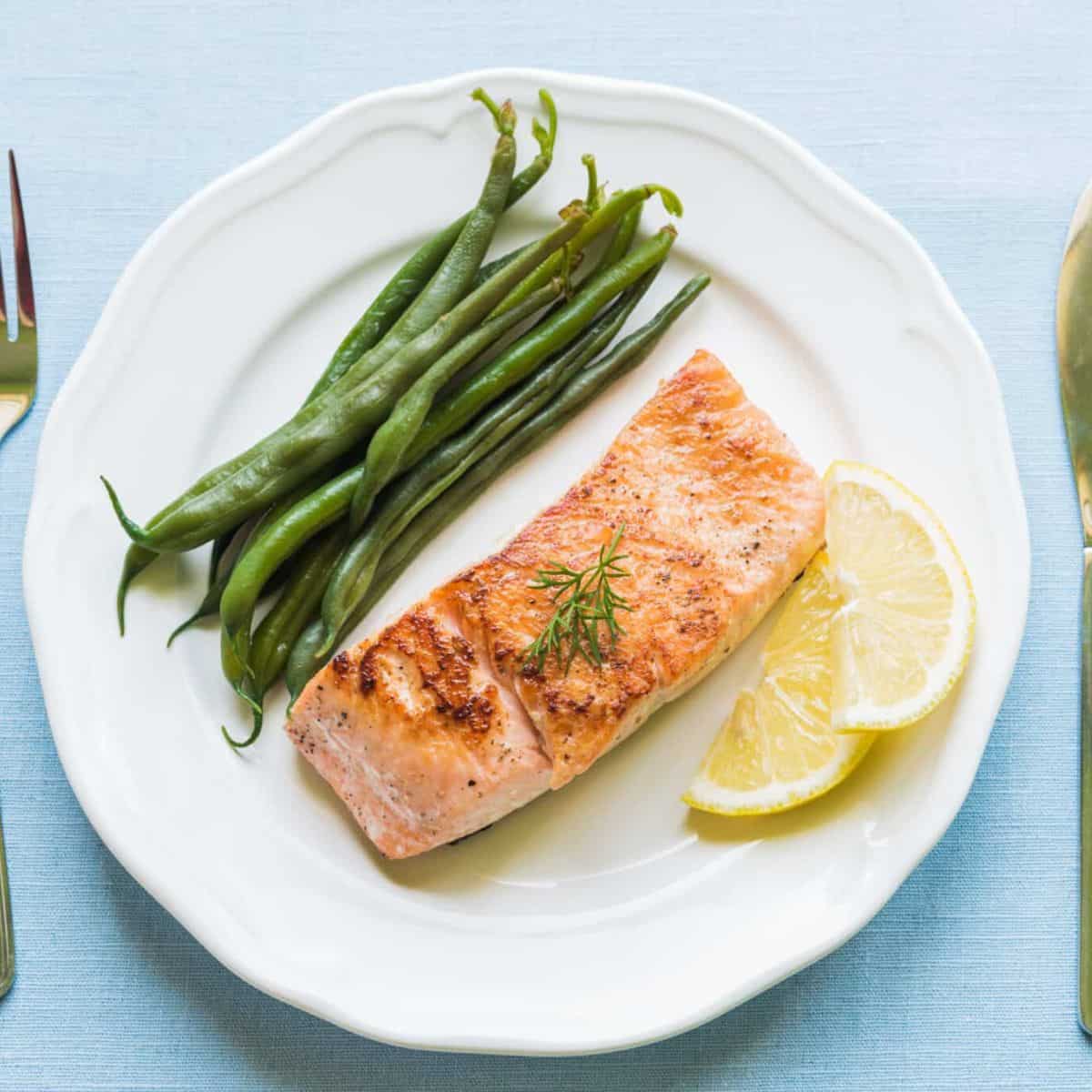 A mouthwatering dish featuring grilled salmon served on a plate with perfectly cooked green beans and a zesty touch of lemon.