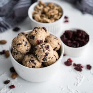 Almond butter balls in a bowls with walnuts and cranberries arranged behind them.