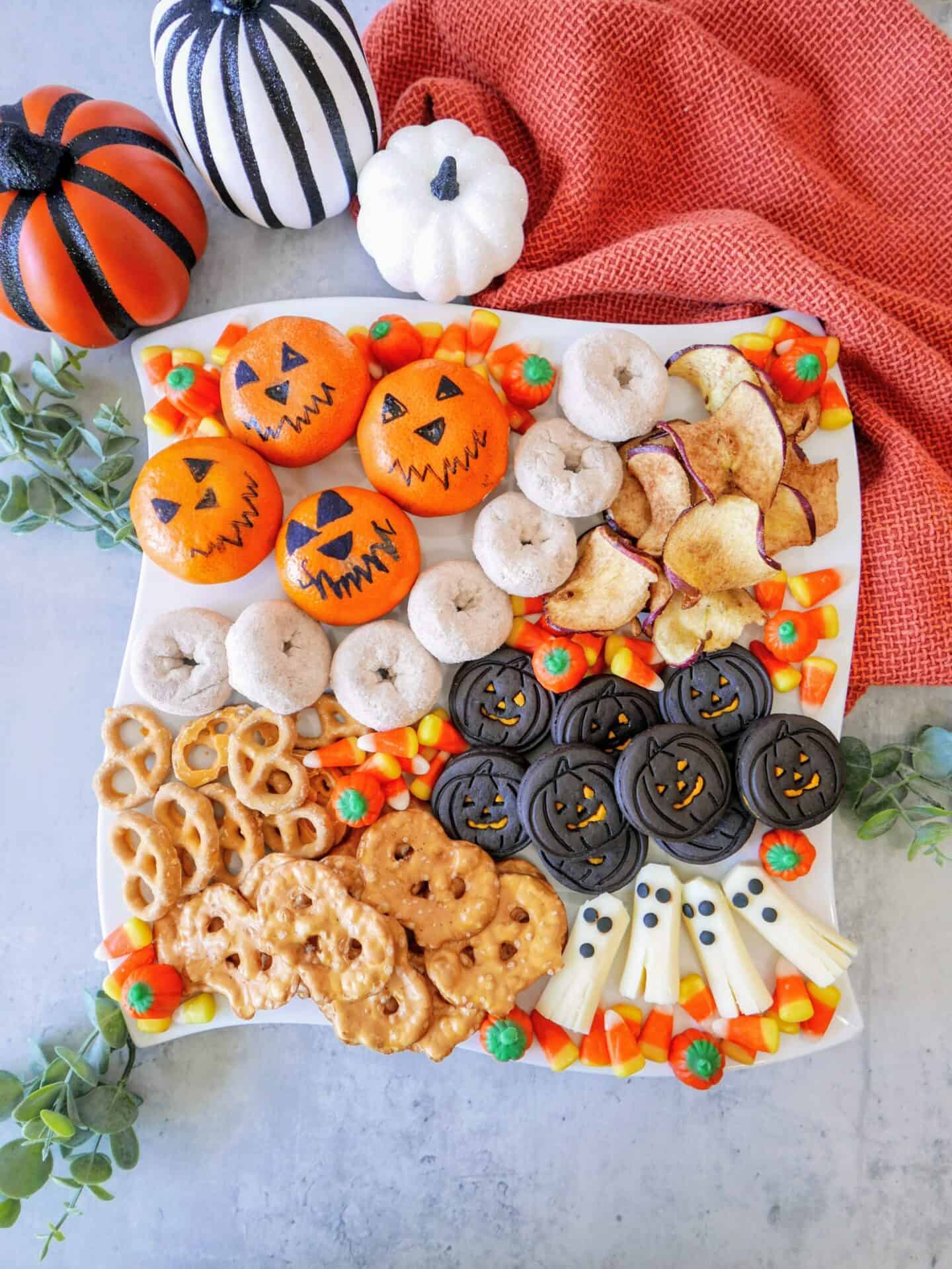 Spooky Halloween snack tray made with oranges, cheese sticks, candy, and cookies. 