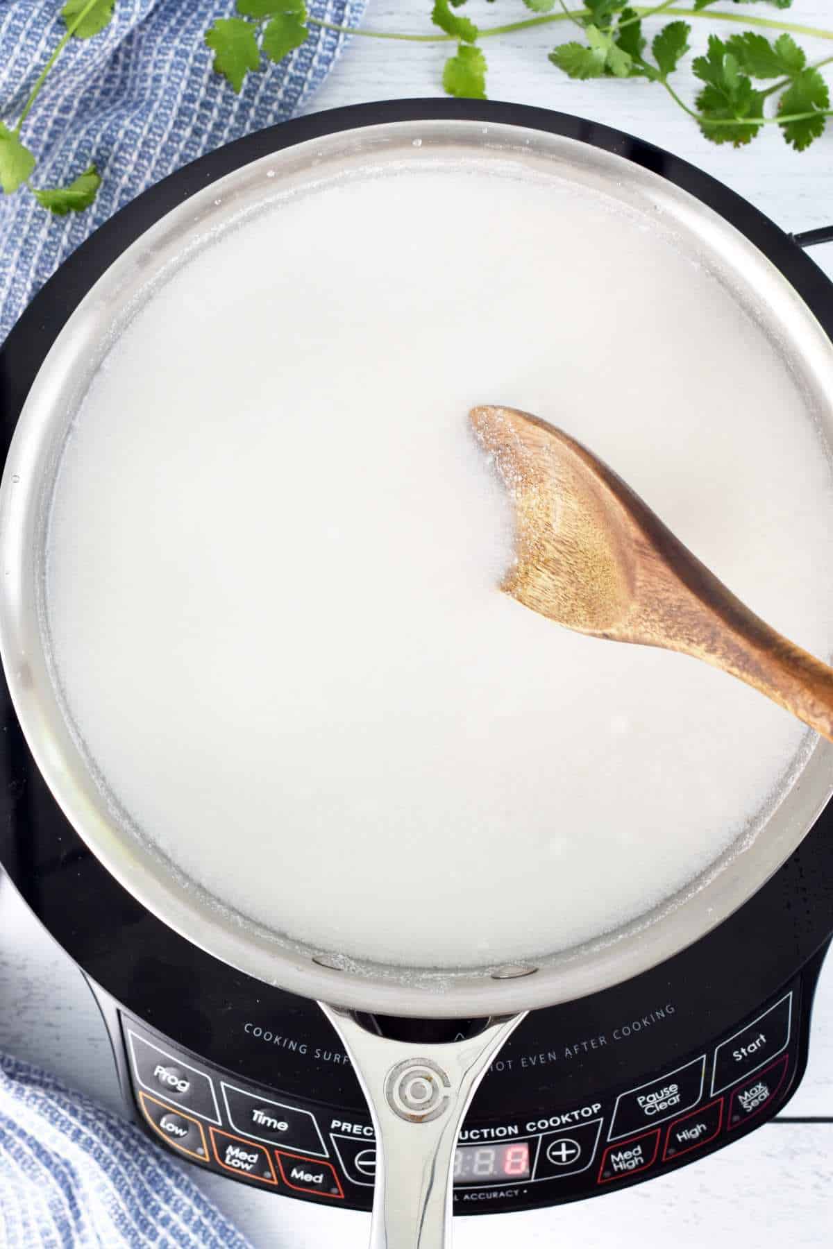 Rice, coconut milk, water, and salt being boiled in a skillet. 