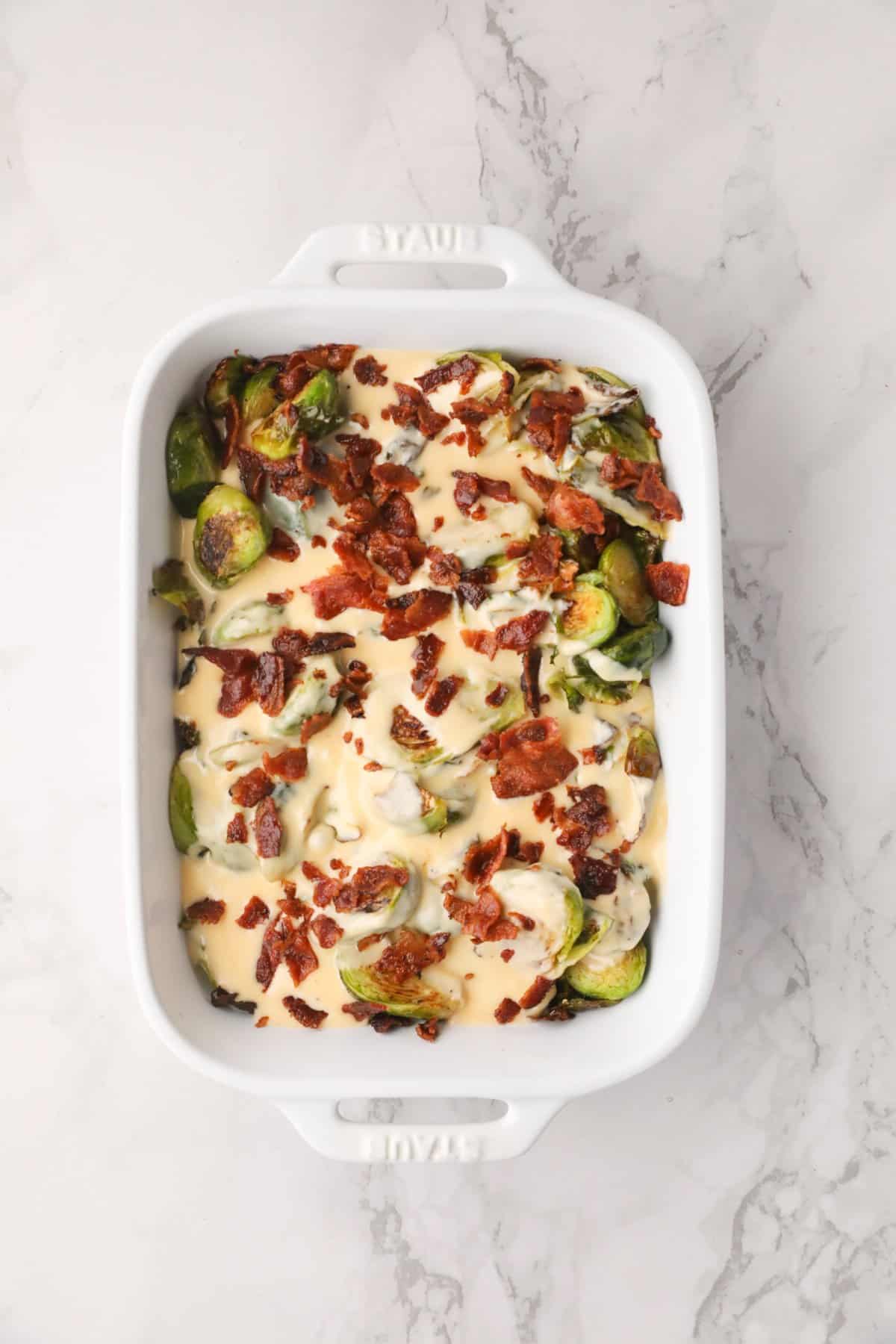 Roasted Brussel sprouts in a pan topped with cream sauce and bacon. 