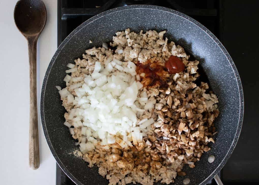 Ground chicken being cooked in a par pan with onion and sauce added. 
