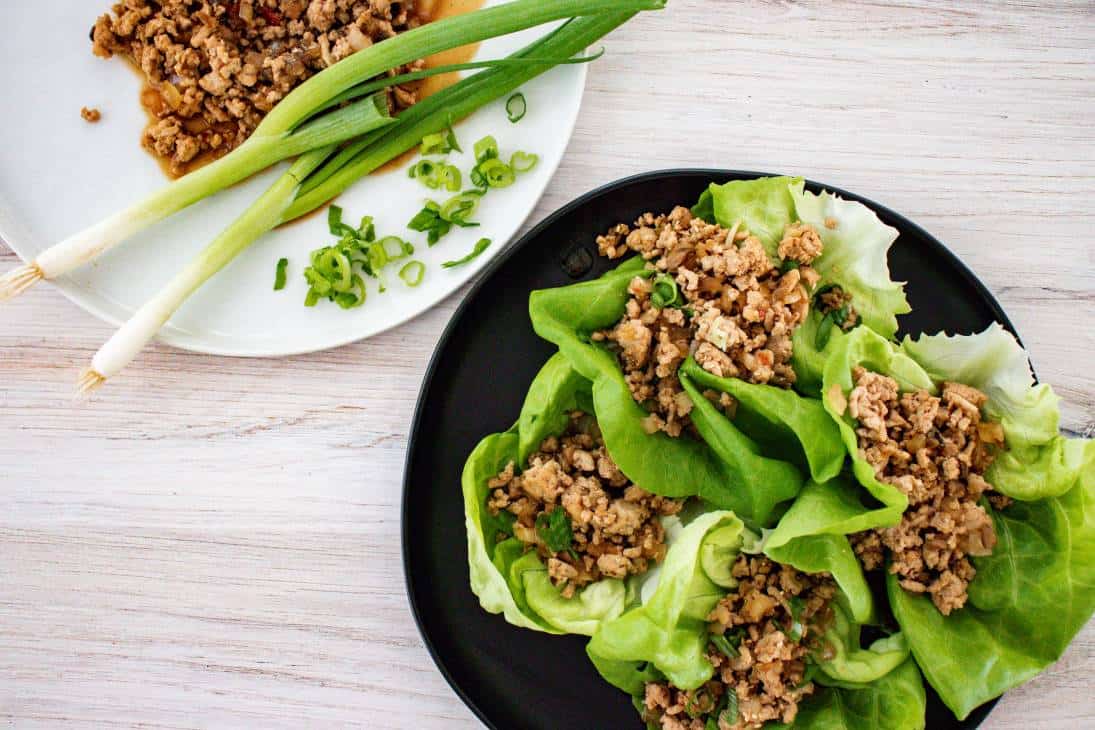Chicken lettuce wraps being served on black plate with green onions sprinkled on top. 