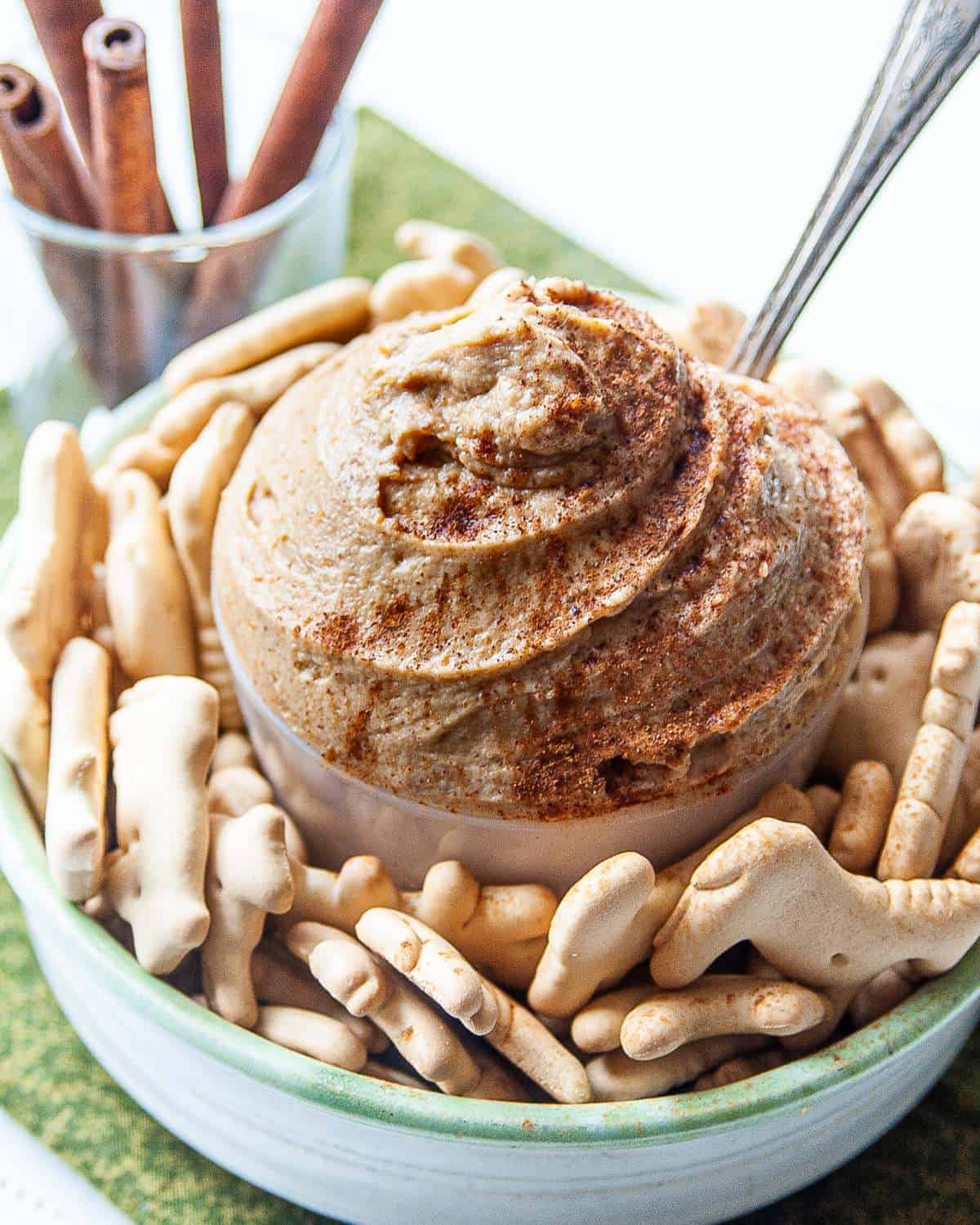 Peanut butter greek yogurt dip in a bowl with a spoon and cinnamon sprinkled on top. 