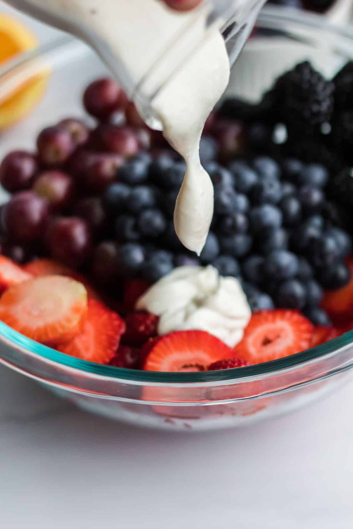 Creamy yogurt dressing being poured over fruit salad. 