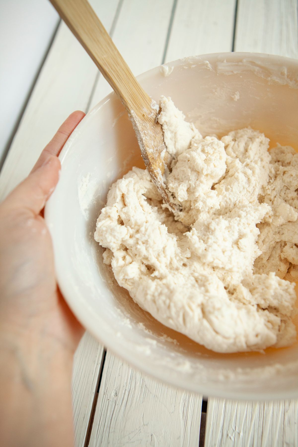 Dough being mixed for biscuits in bowl with a wooden spoon. 