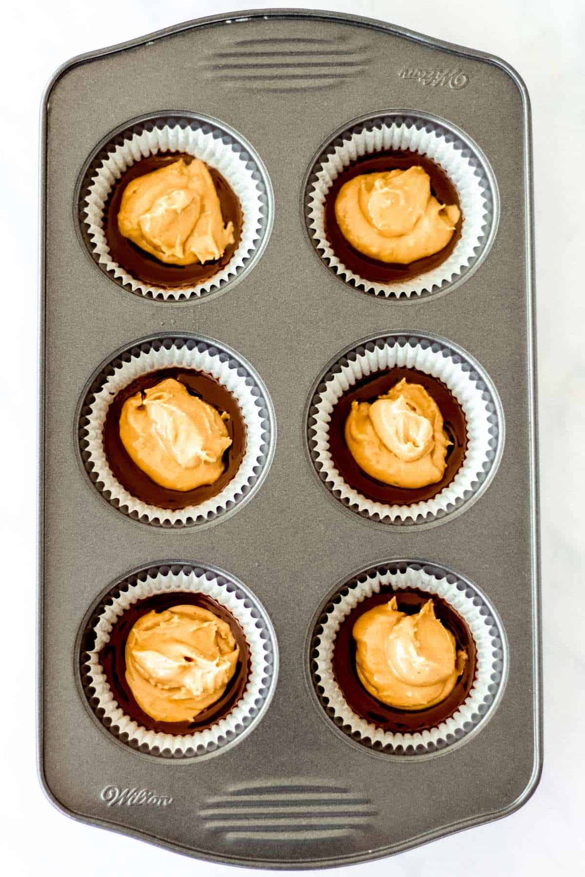 Peanut butter mixture on top of chocolate mixture in muffin tins. 