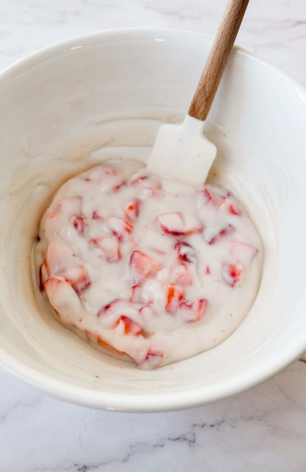 Strawberries, greek yogurt, honey, whipped topping, and vanilla being mixed together in a bowl. 
