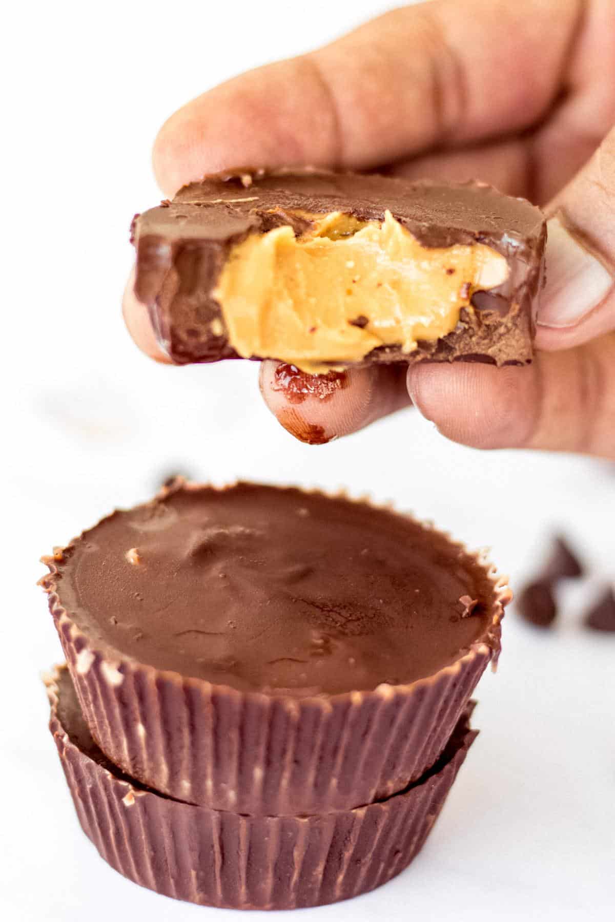Dark chocolate peanut butter cup being held with a bite taken out of it. 