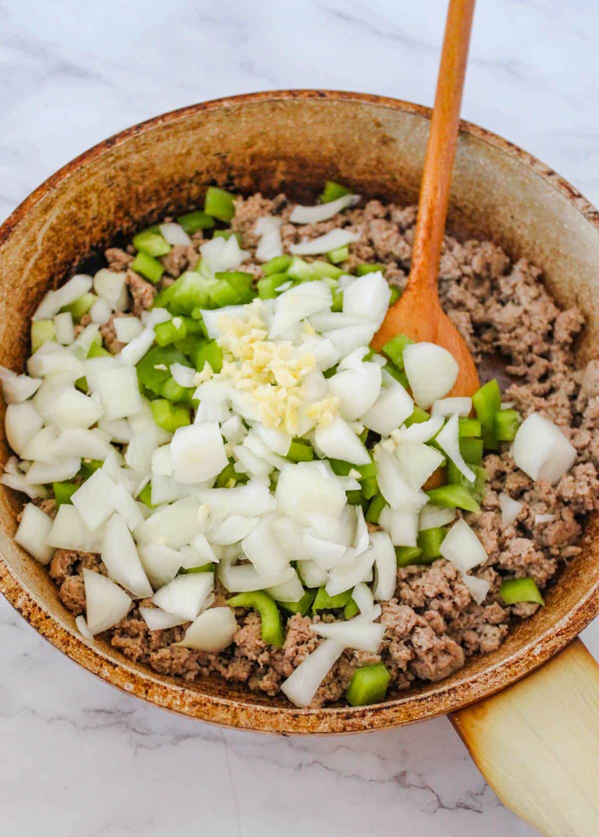 Ground turkey, garlic, onions, and green bell peppers being cooked in a skillet. 