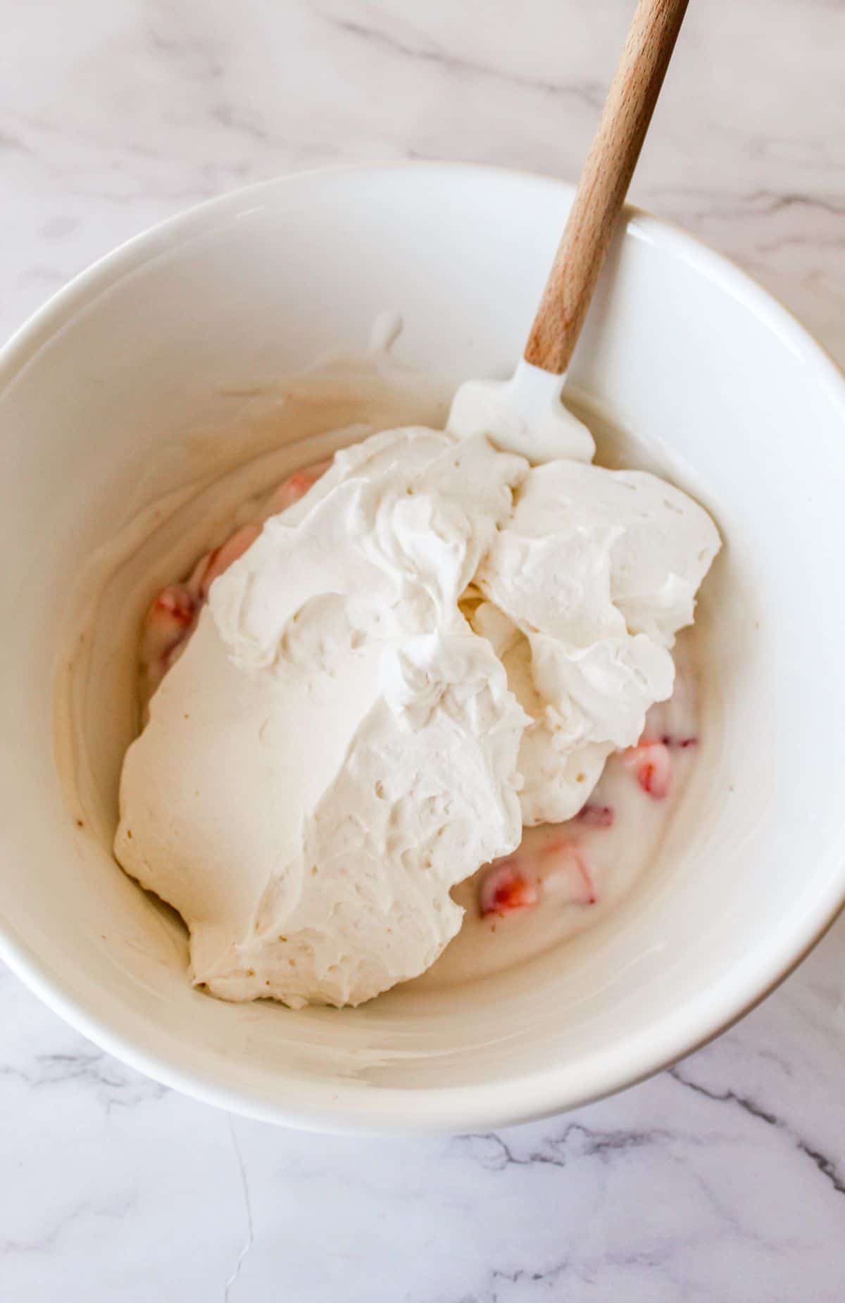 Whipped topping being folded into the greek yogurt mixture in a bowl. 