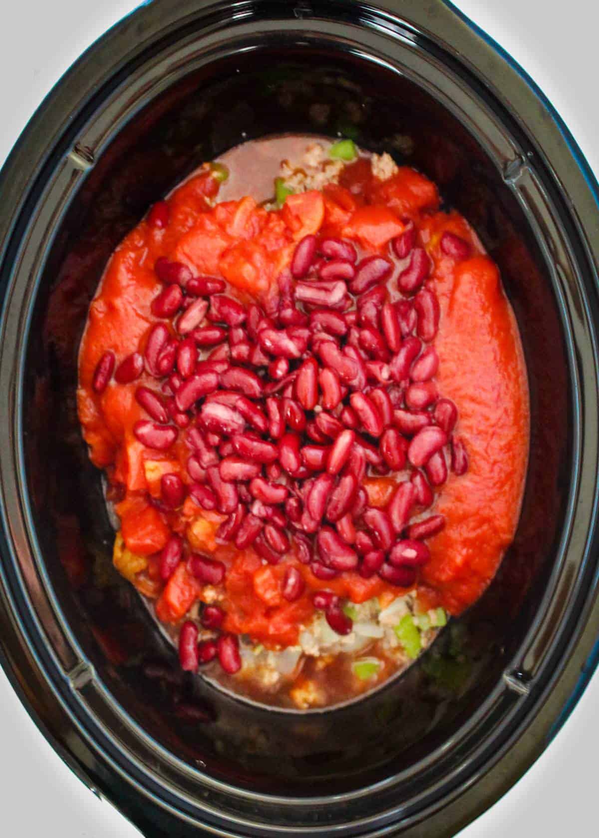 Ground turkey, kidney beans, diced tomatoes, onions, in a crock pot ready to be cooked. 
