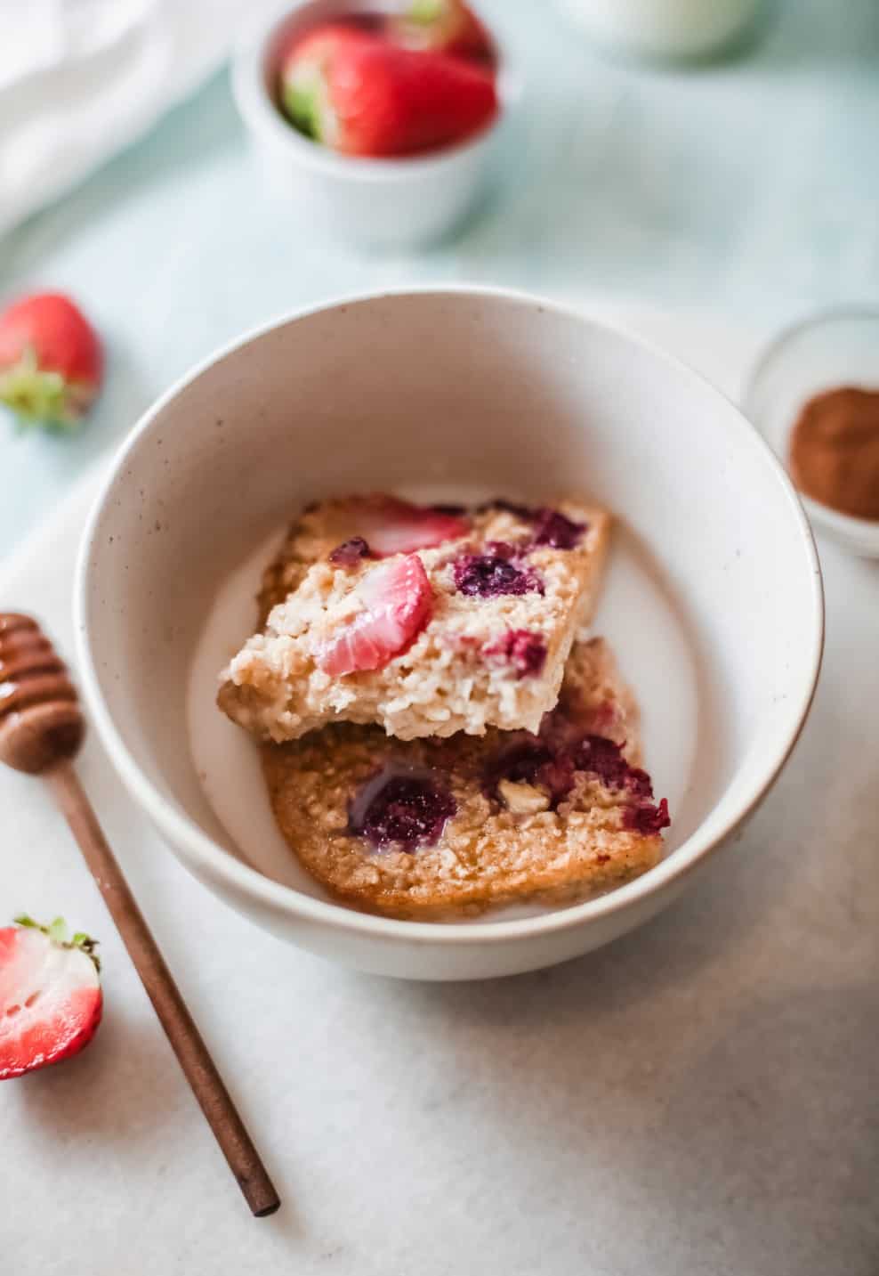 Mixed berry oatmeal bars cut into sliced and being served in a bowl with milk. 