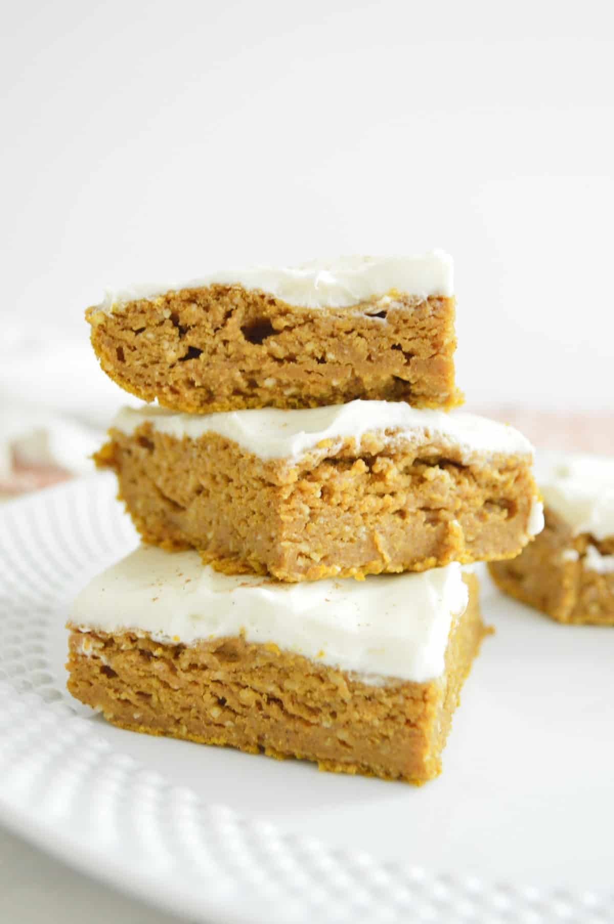 Healthy pumpkin bars with cream cheese frosting being stacked on top of each other. 