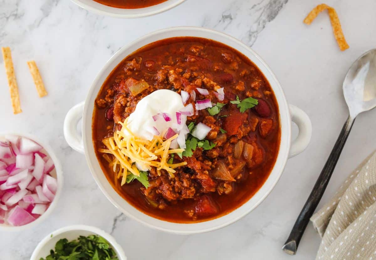 Macro friendly turkey chili being served out of a white bowl with toppings around it. 