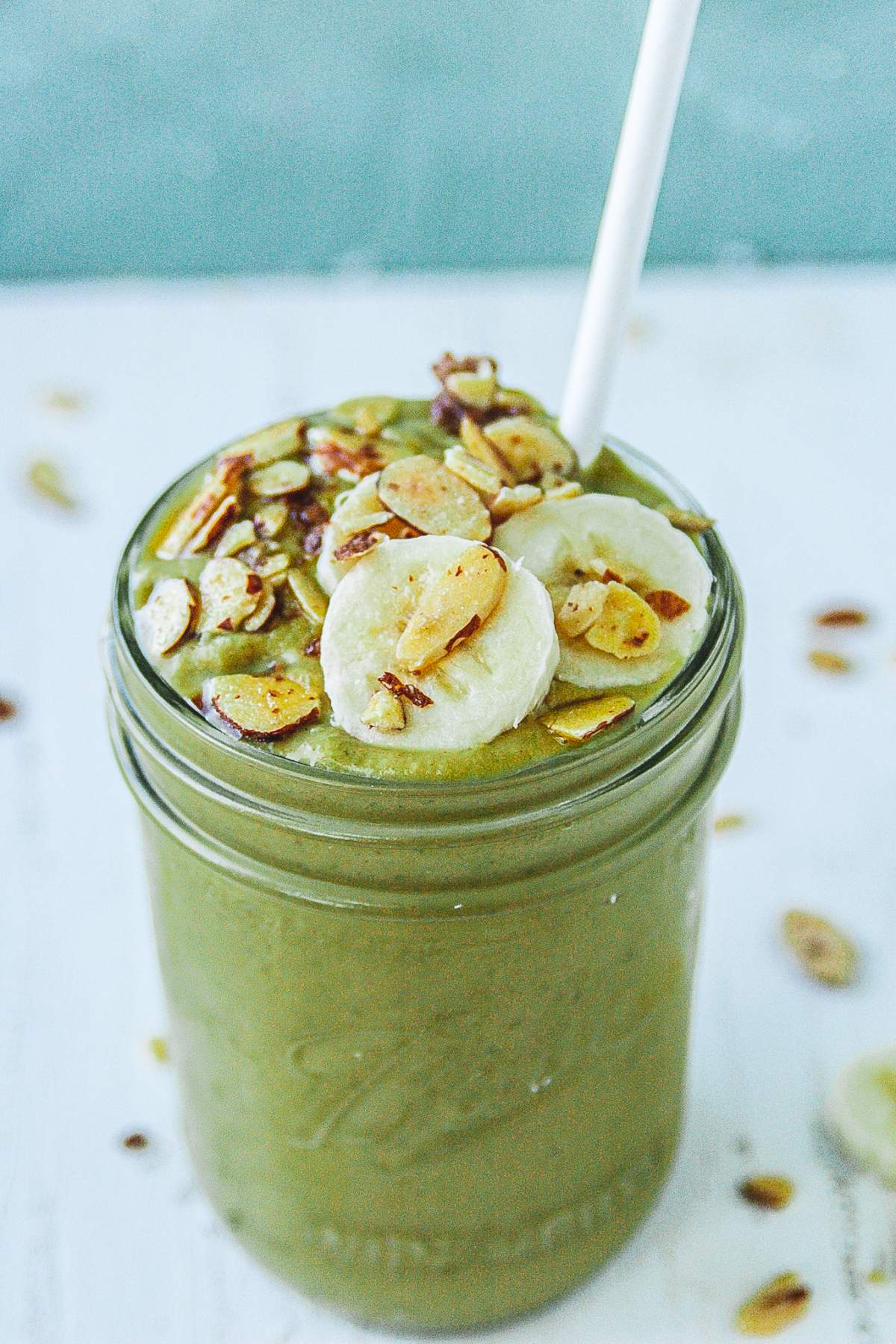 Mango spinach smoothie in a mason jar topped with banana and sliced almonds. 