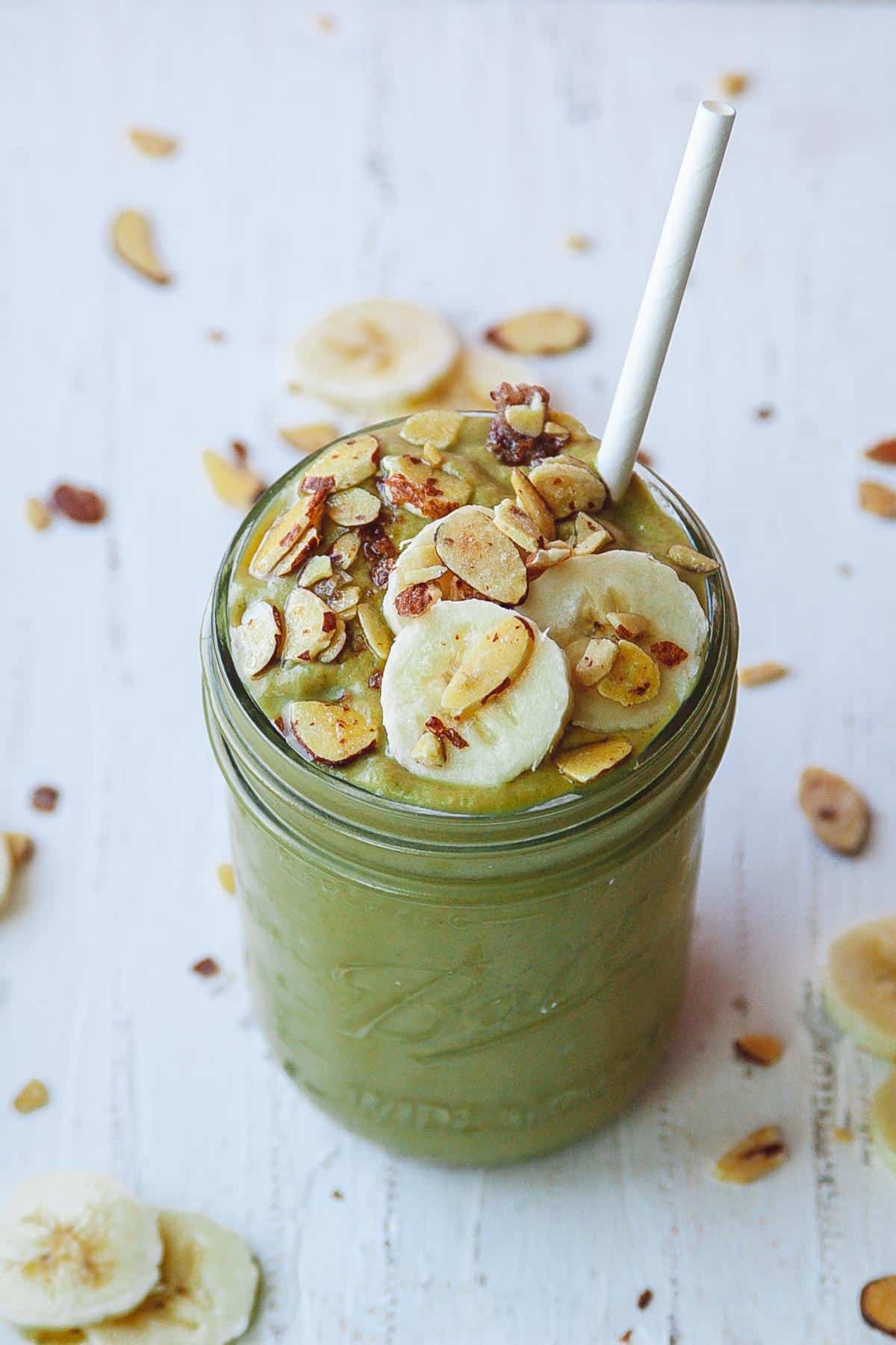 Spinach Mango smoothie in a mason jar with banana and almonds spread around it. 