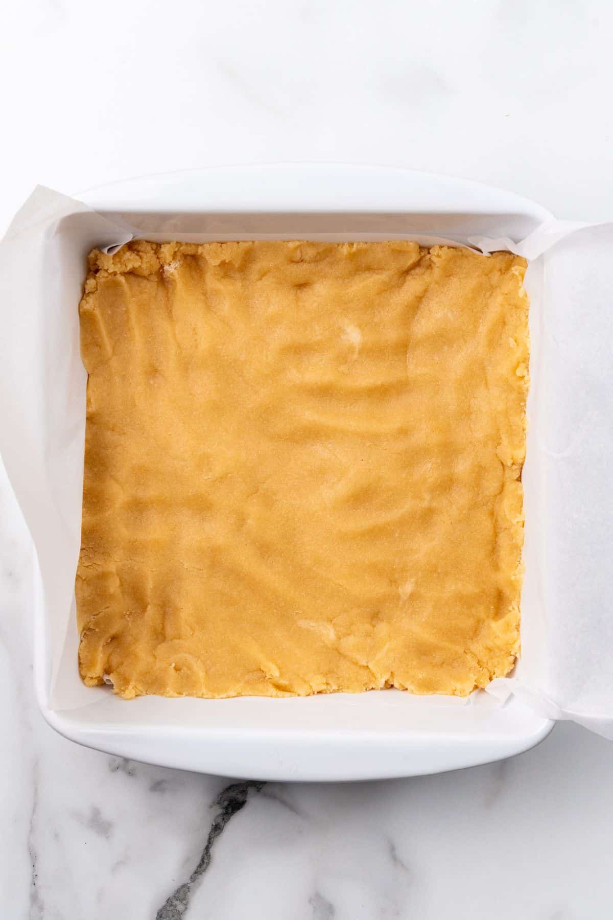Shortbread layer being pressed into a white pan. 