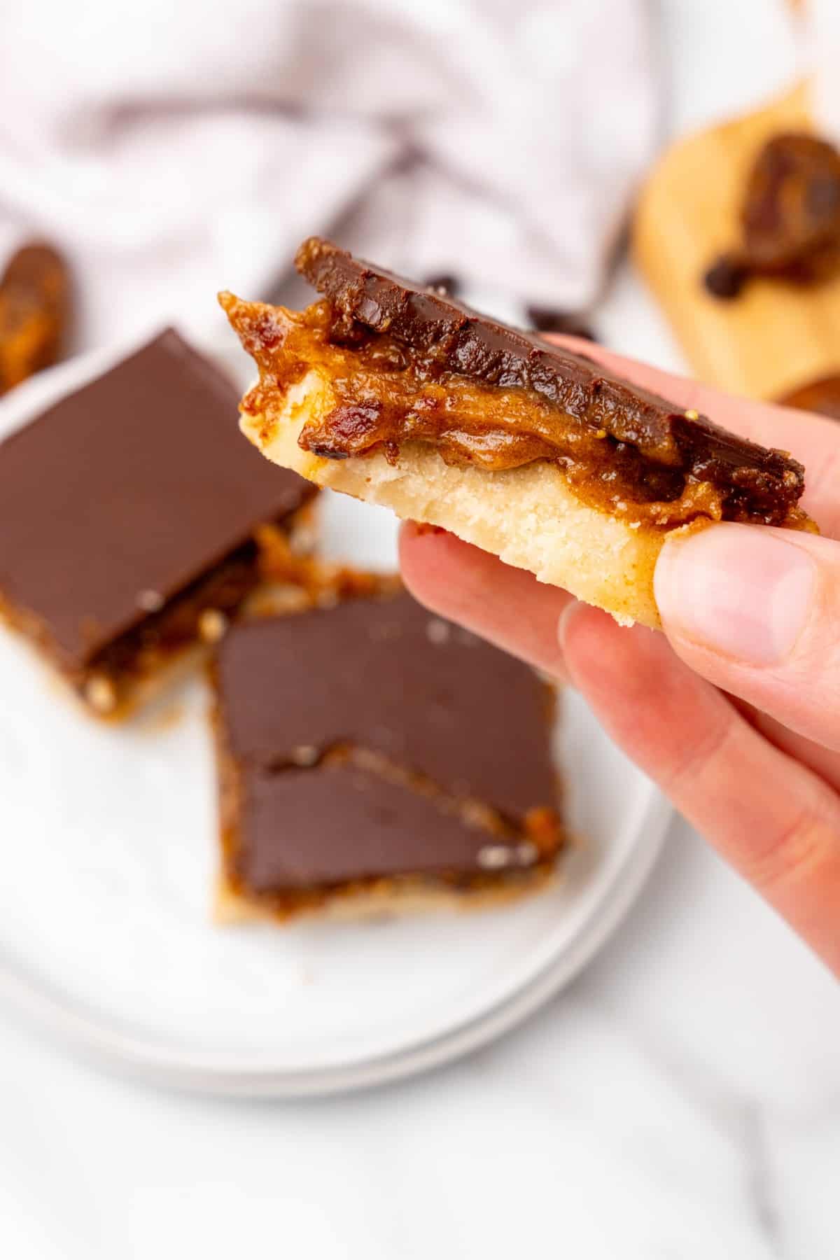 Millionaire shortbread being held with a bite taken out of it. 