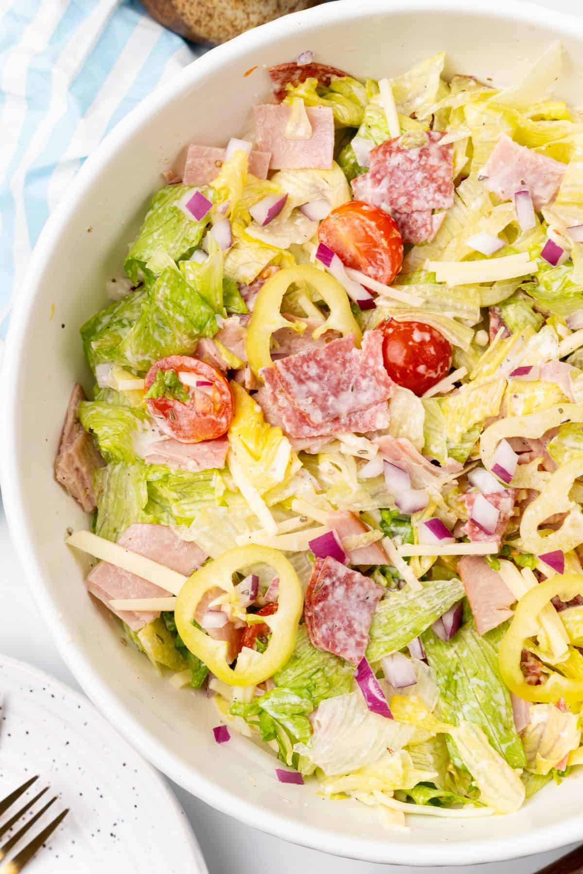 A grinder salad topped with ham, salami, and tomatoes.