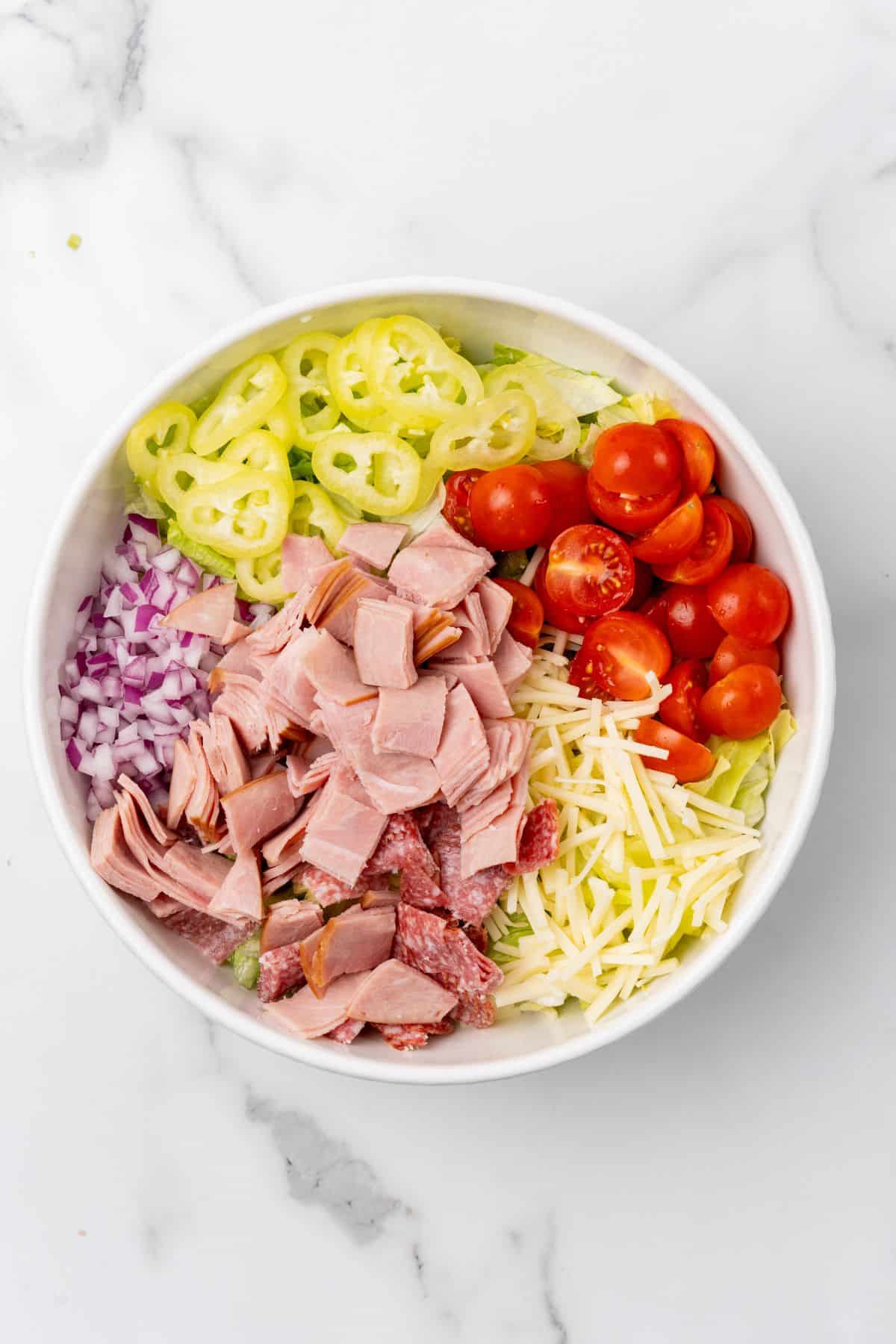A salad bowl with ham, lettuce, tomatoes, and salami. 