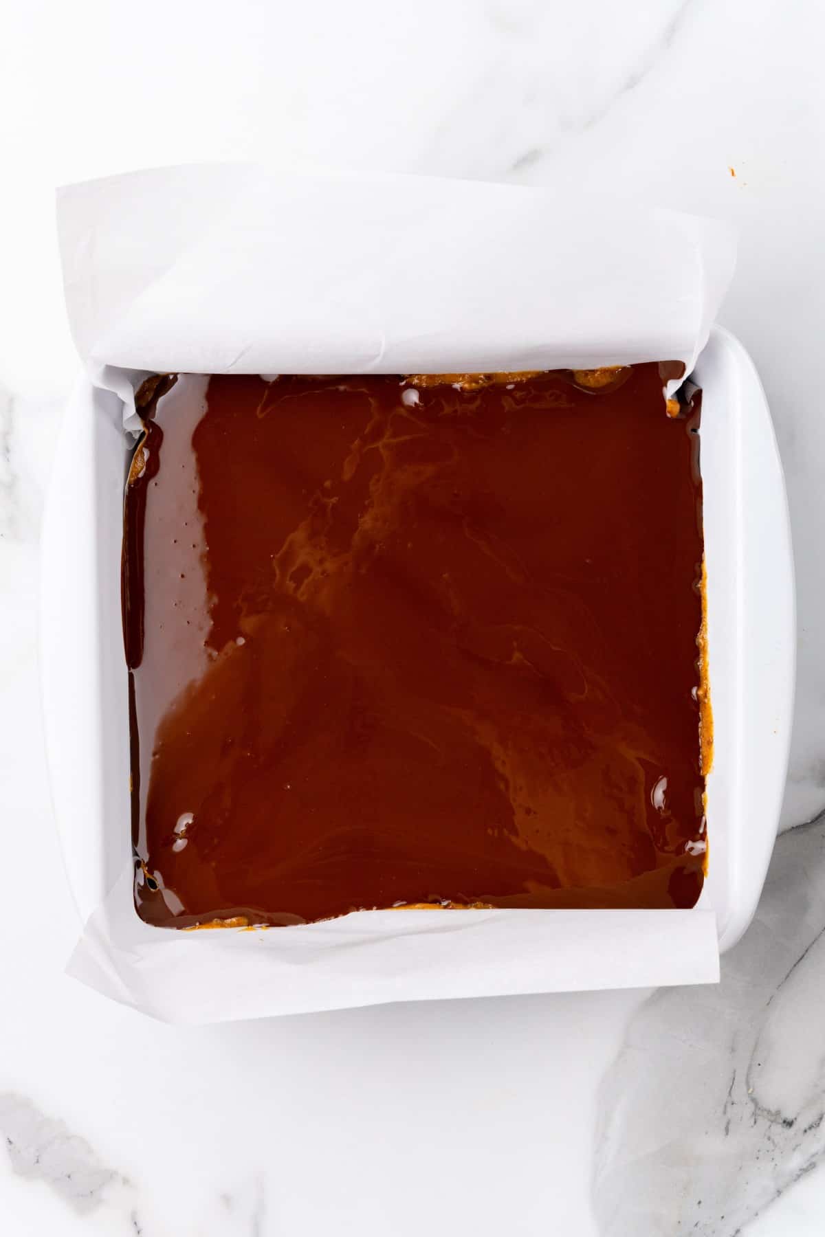 Melted chocolate being spread into white baking pan. 
