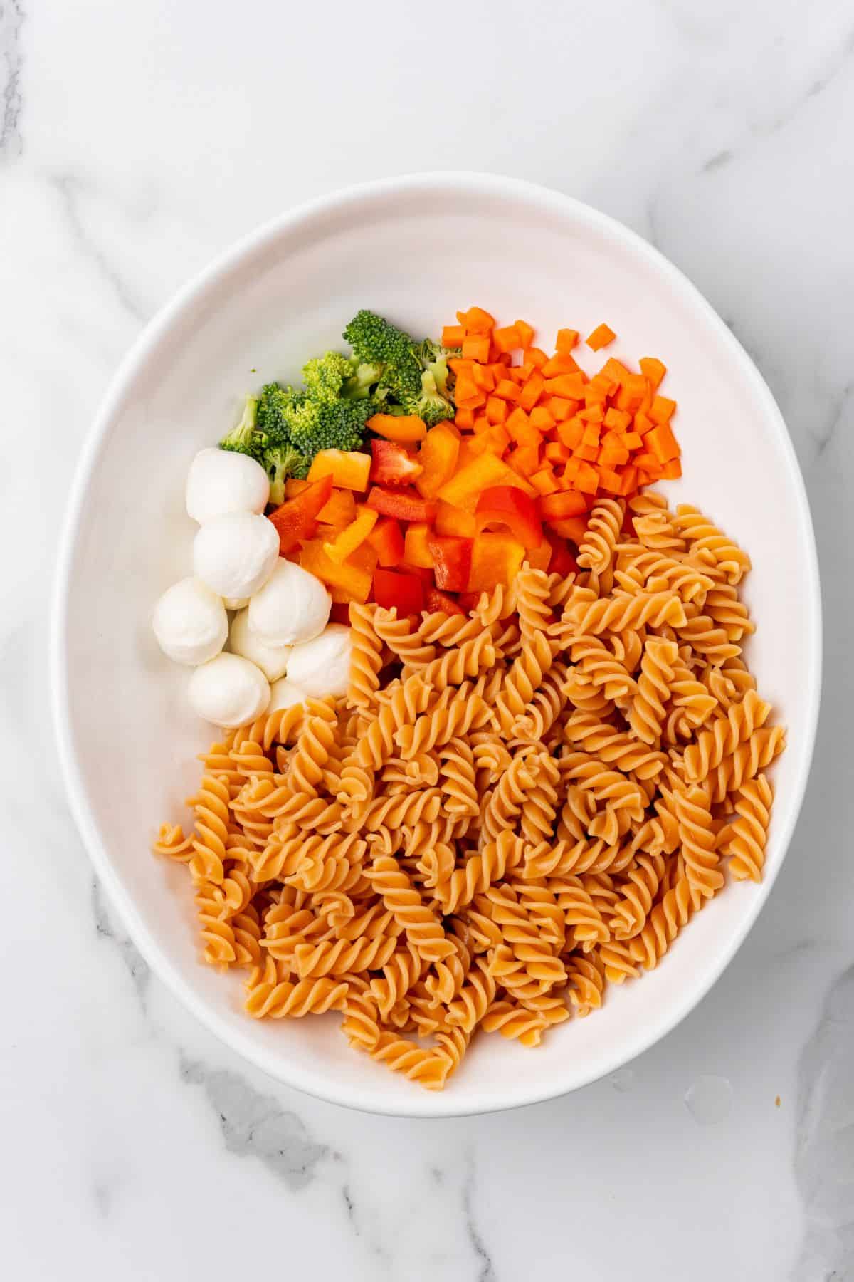 A protein-packed pasta salad with carrots, broccoli, and bell peppers, and mozzarela cheese. 
