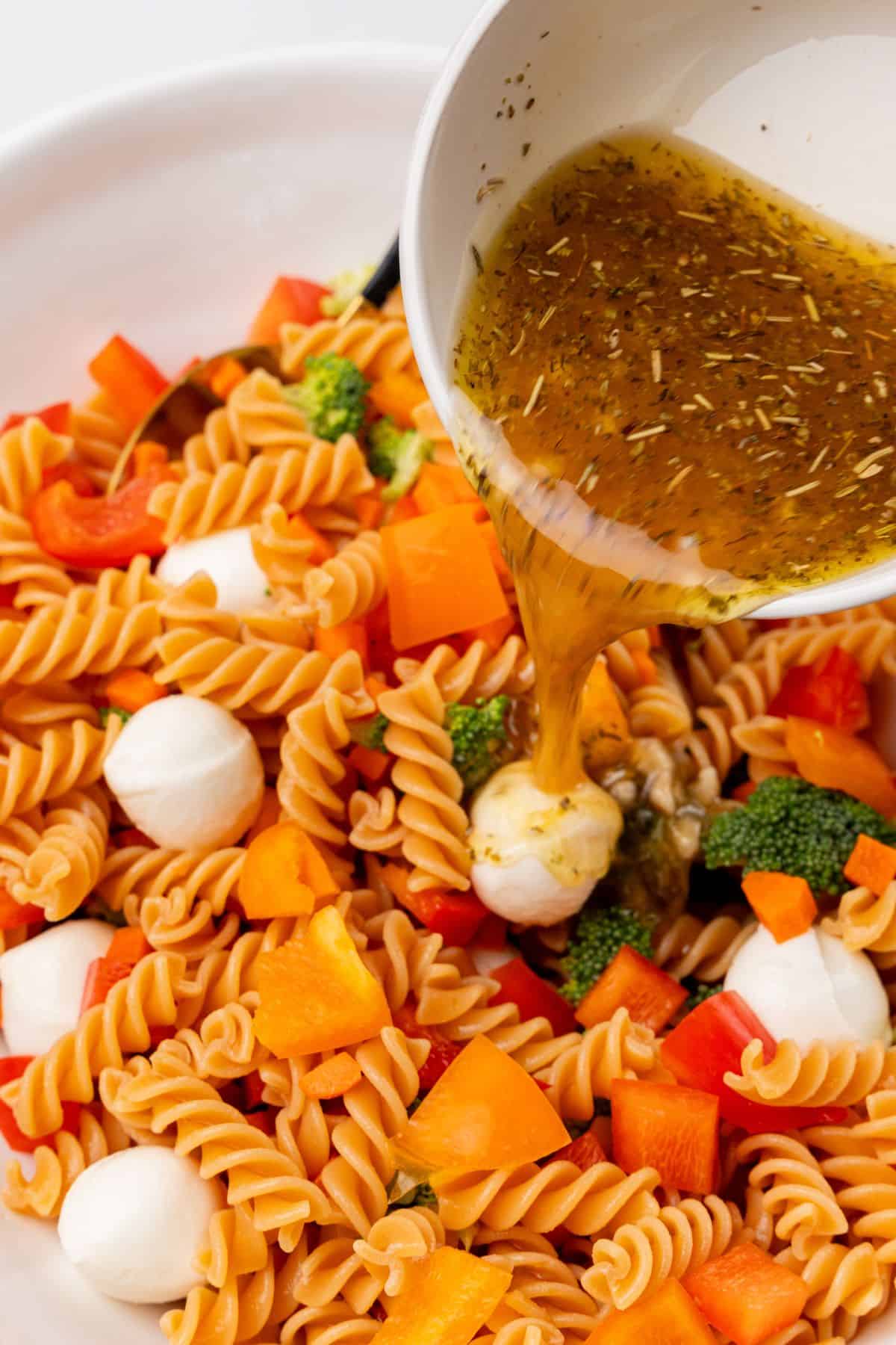 A protein-packed pasta salad with dressing being poured on top. 