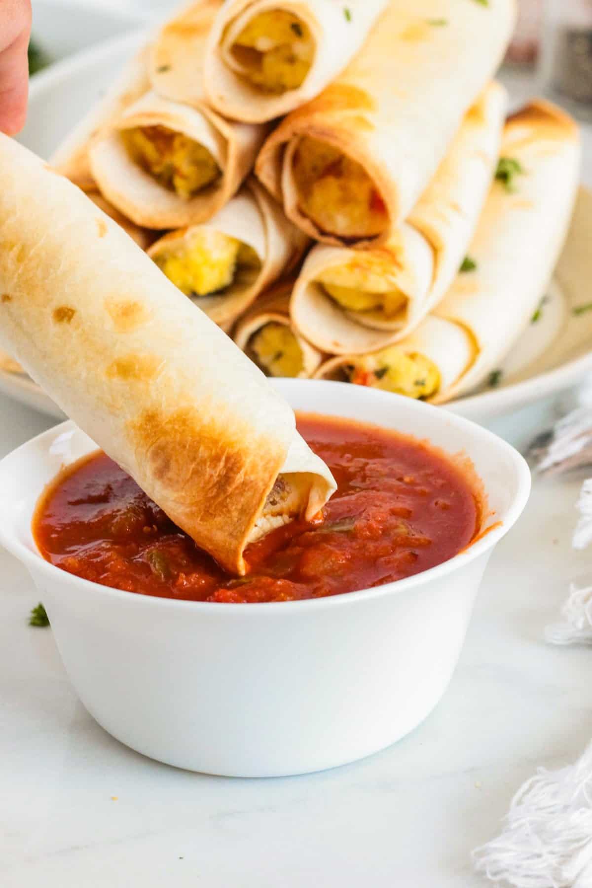 A person dipping Breakfast Taquitos into salsa. 