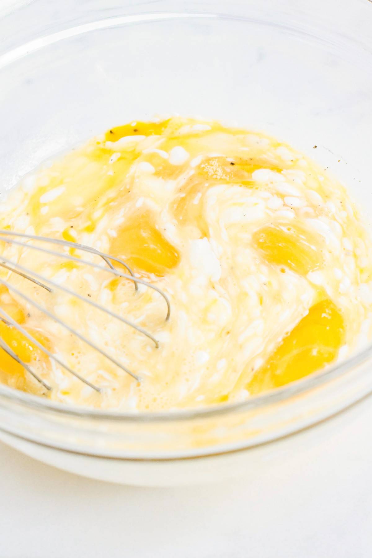 A bowl of scrambled eggs with a whisk in it.