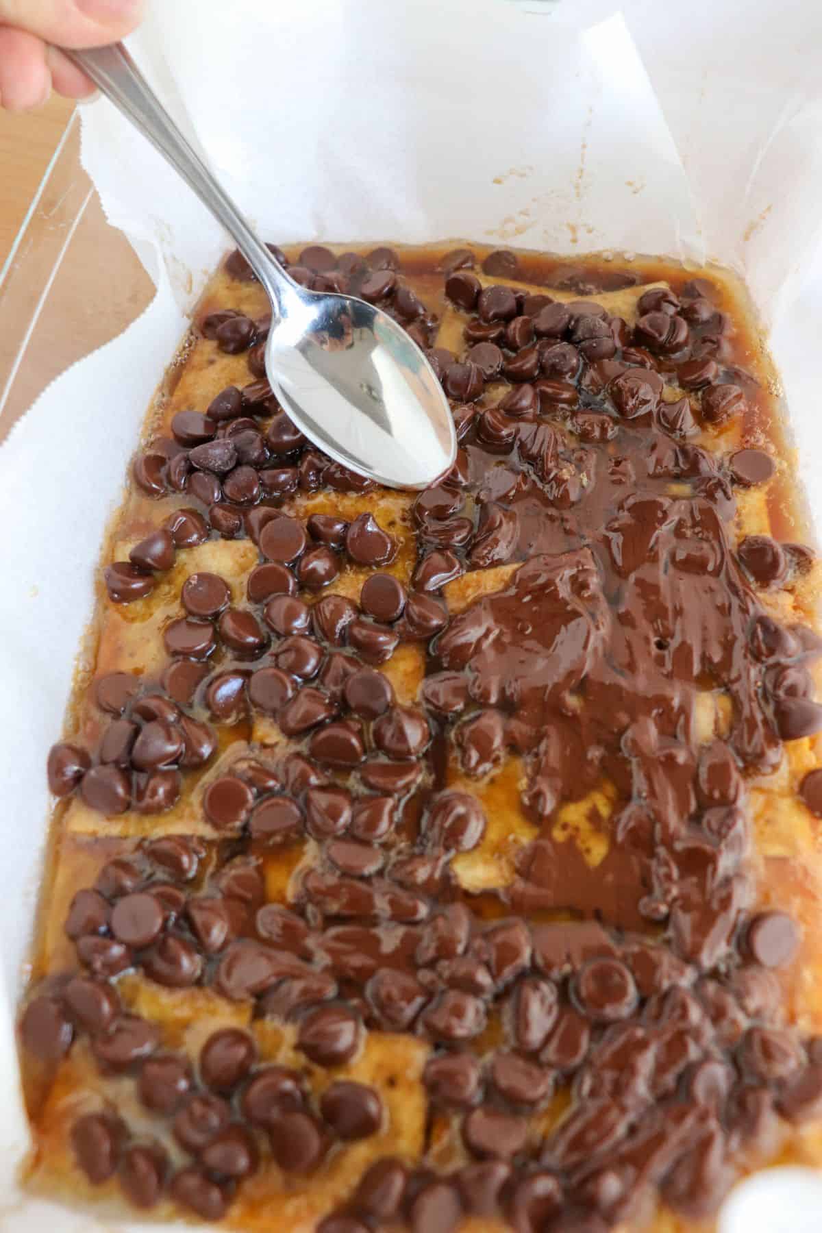 A spoon being used to spread melted chocolate chips over keto christmas crack. 