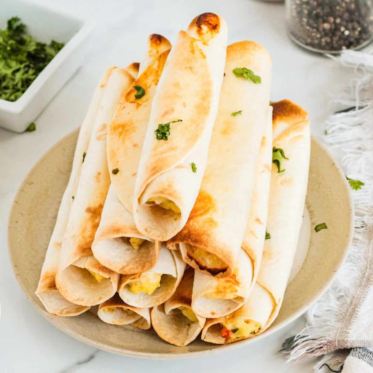 A plate with a stack of breakfast taquitos.