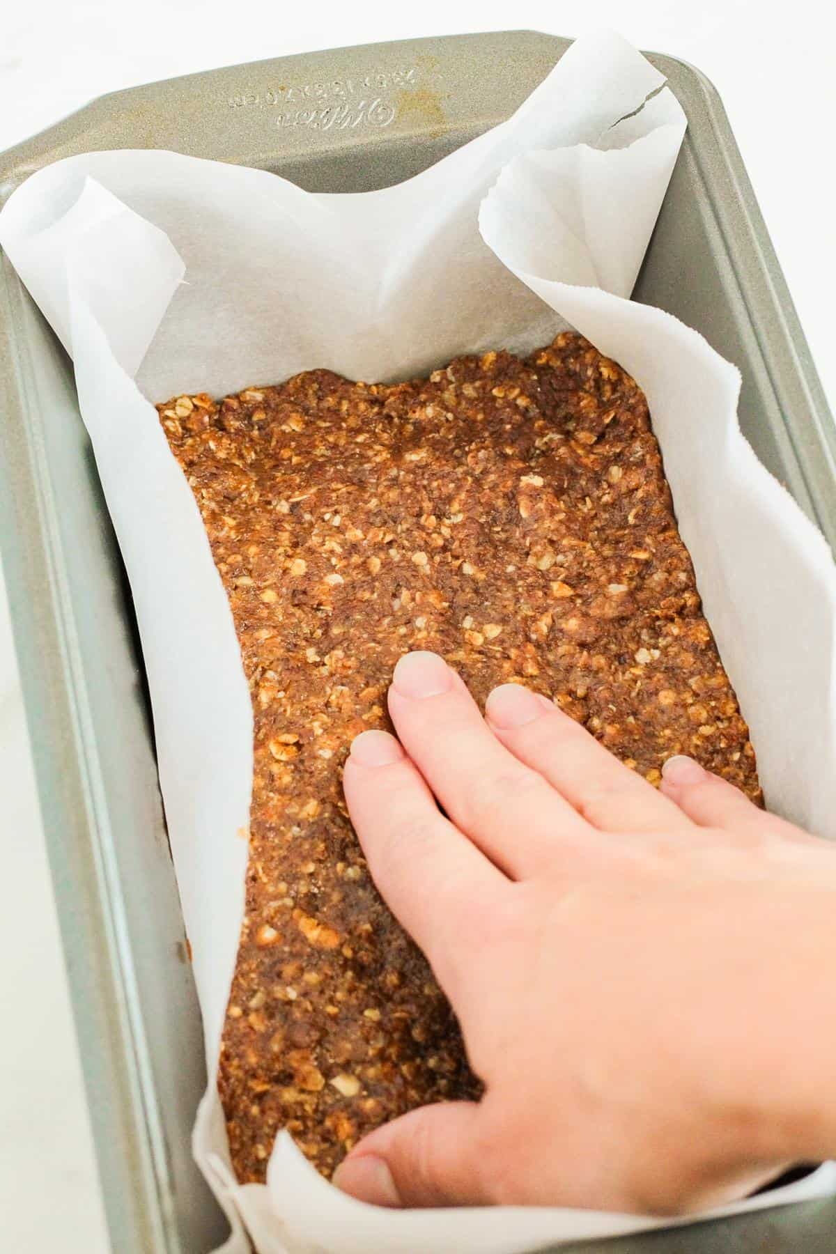 A hand reaching into a pan of Pumpkin Protein Bars to flatten it. 
