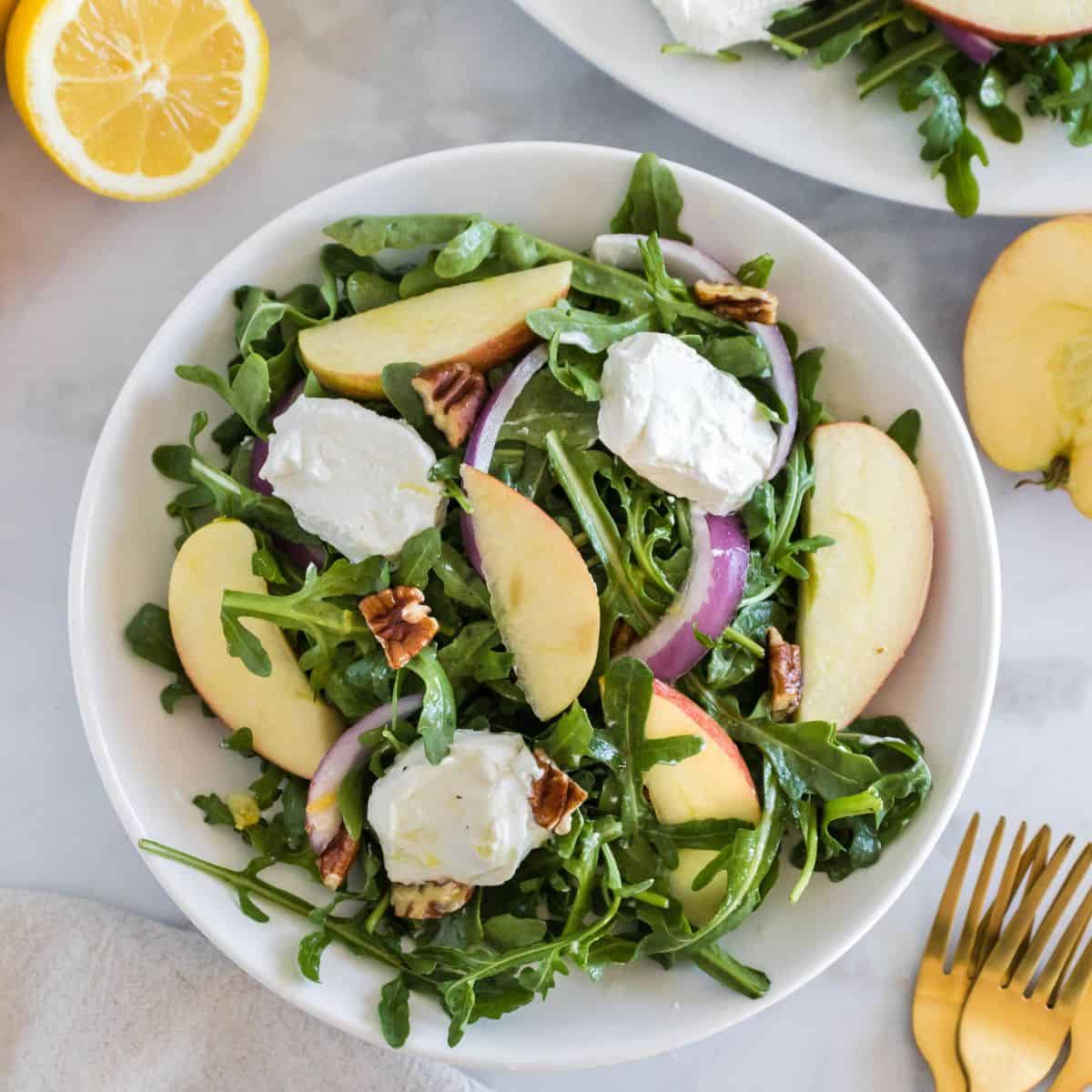 A bowl of arugula salad with apples and goat cheese.
