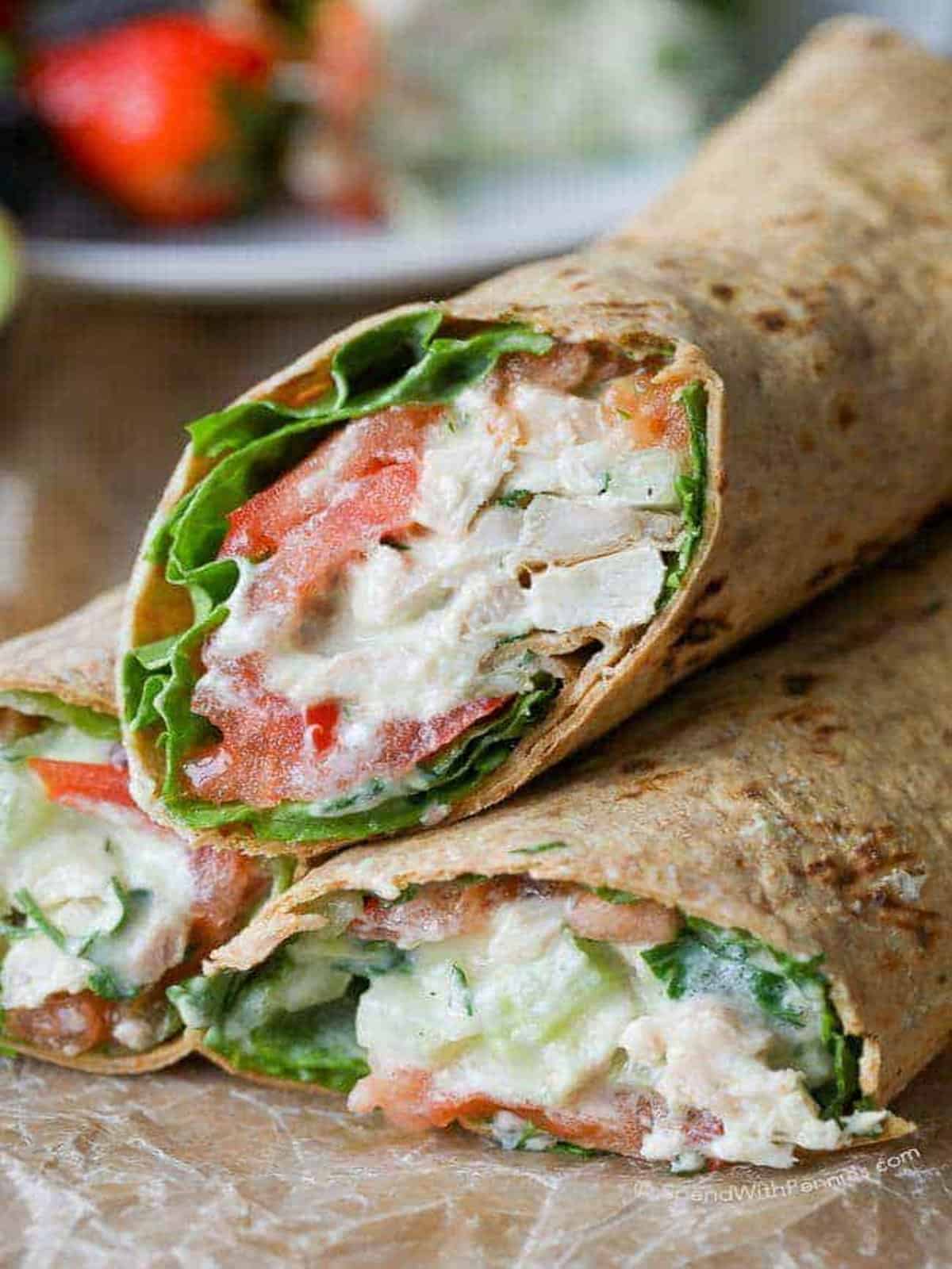 An avocado ranch chicken salad wrap with chicken, lettuce, and tomatoes on a piece of parchment paper. 