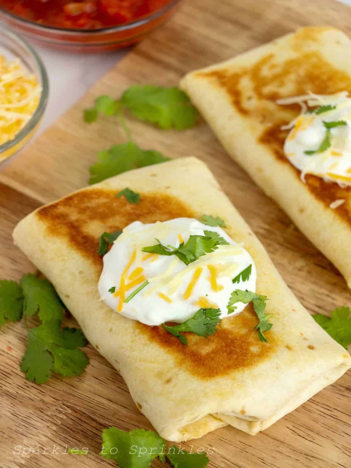 Two crispy chicken salsa wraps with sour cream and cilantro on a cutting board.