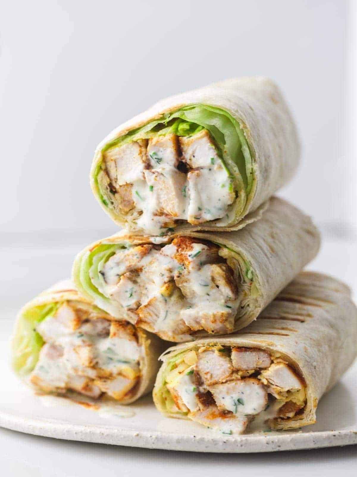 Four healthy grilled chicken wraps stacked on a plate.