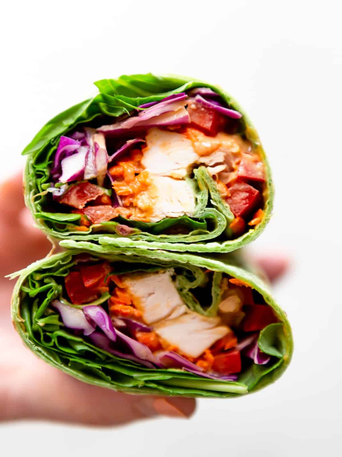 A person holding a peanut chicken wrap packed with vibrant lettuce and fresh vegetables.
