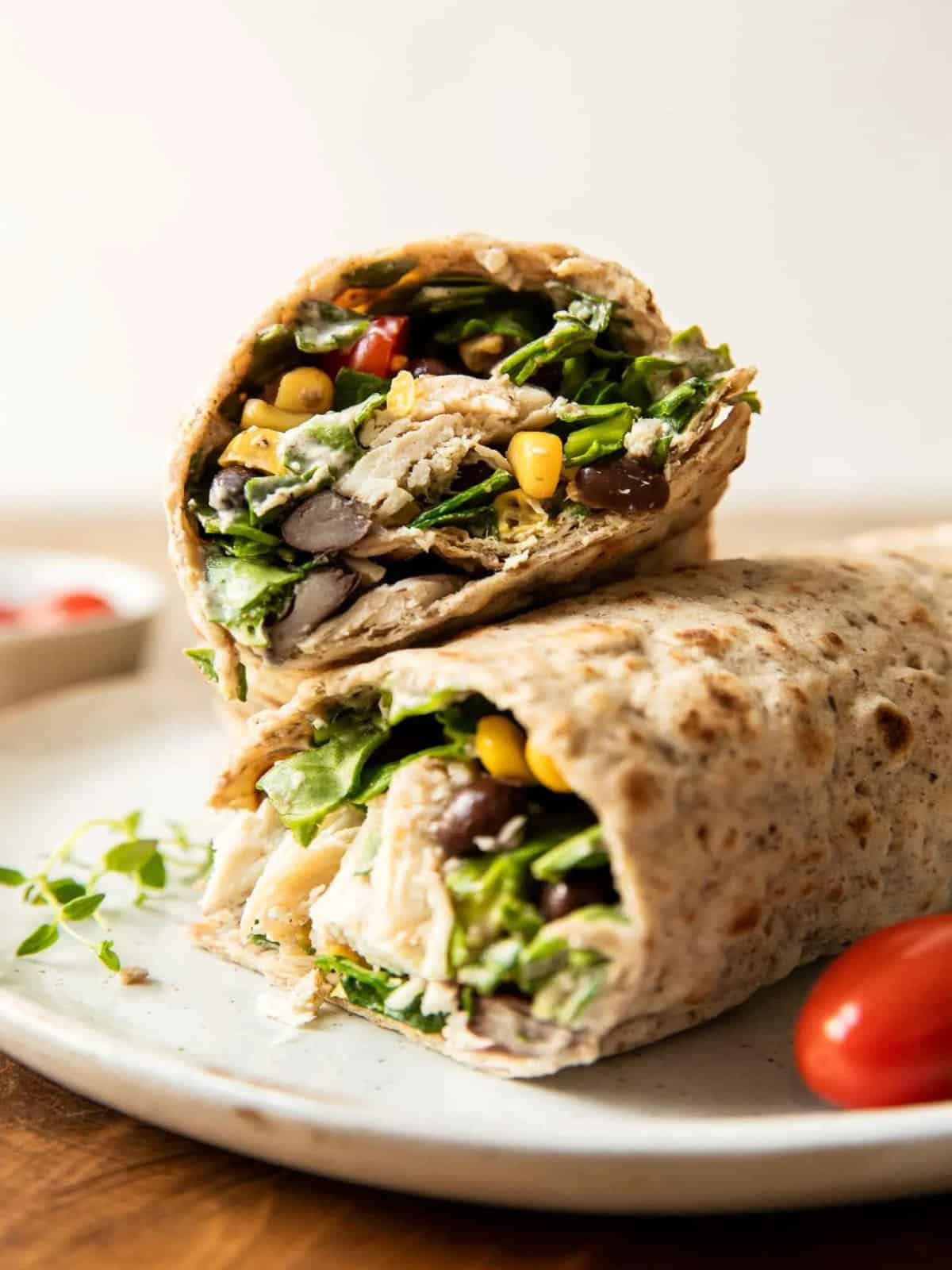 A fiesta ranch chicken wrap made with corn and black beans on a plate with tomatoes. 