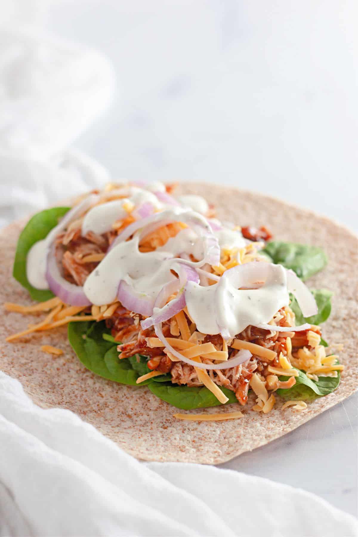 A wrap filled with BBQ chicken, red onions, ranch dressing, spinach, and cheese.