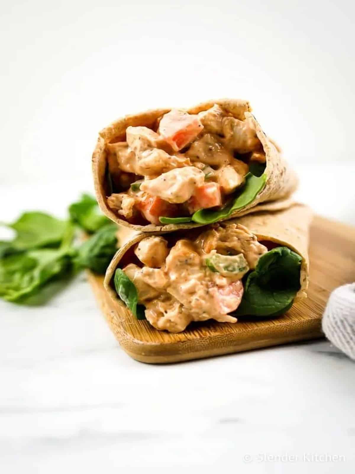 Buffalo ranch chicken wraps on a wooden cutting board with lettuce. 