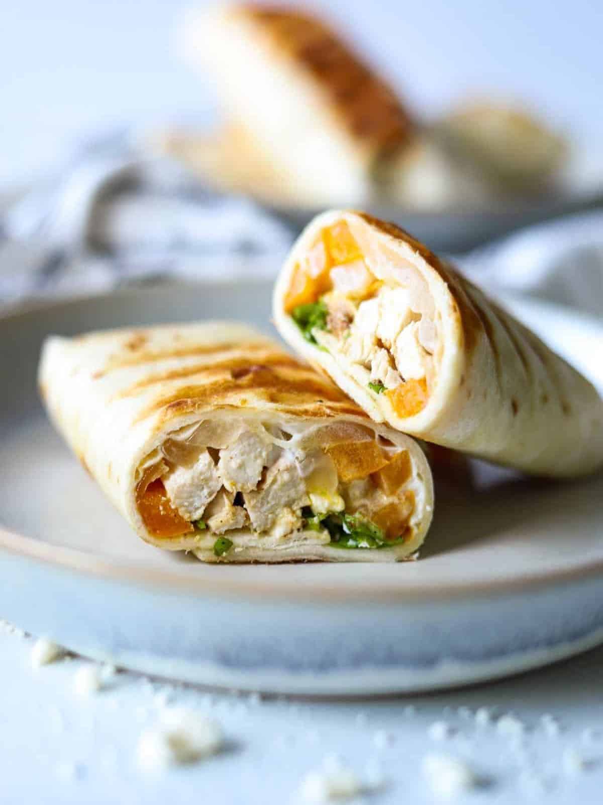 A white plate with two healthy chicken fajita wraps on it.