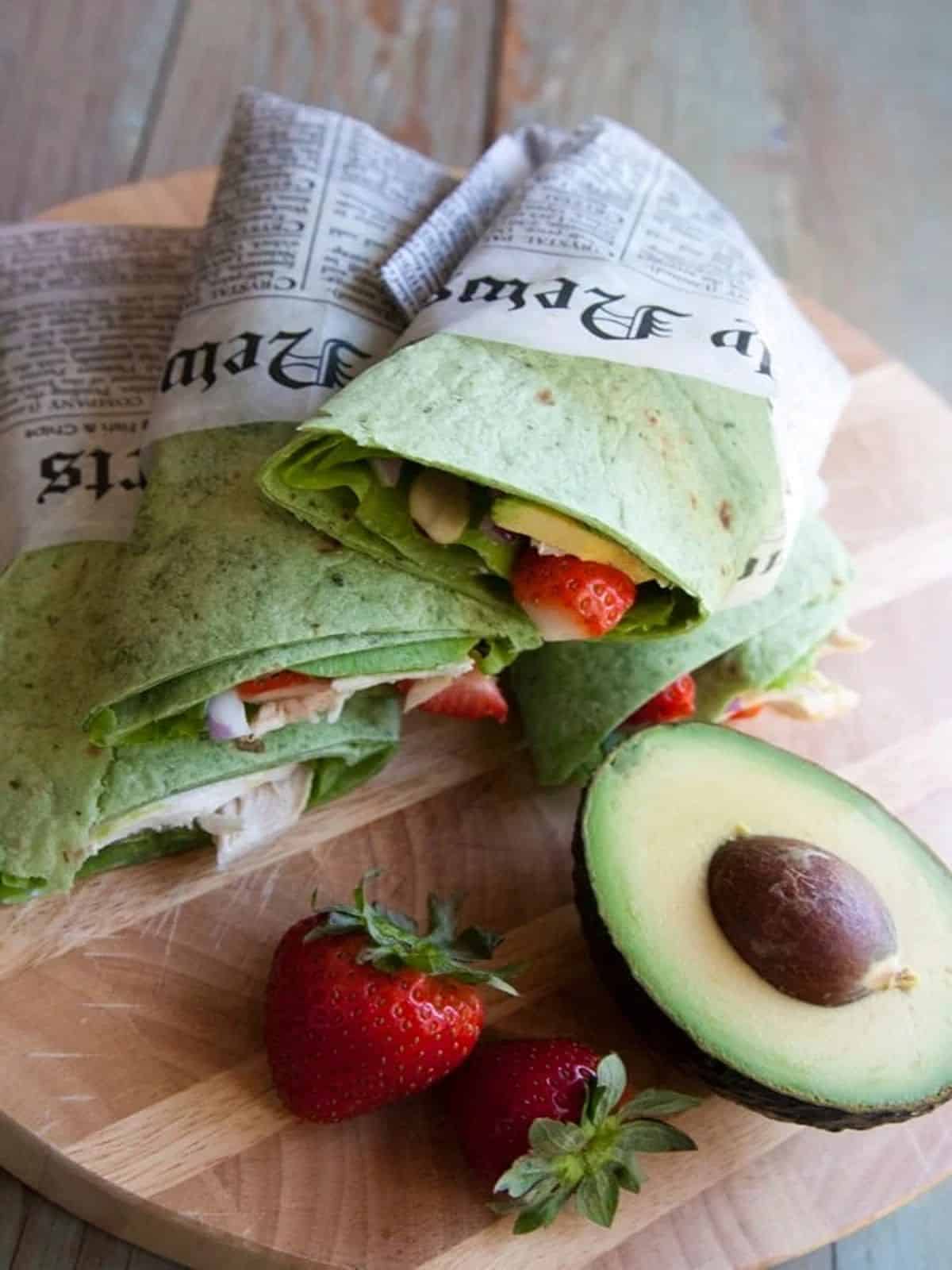 A chicken salad strawberry wrap with strawberries and avocado on a cutting board