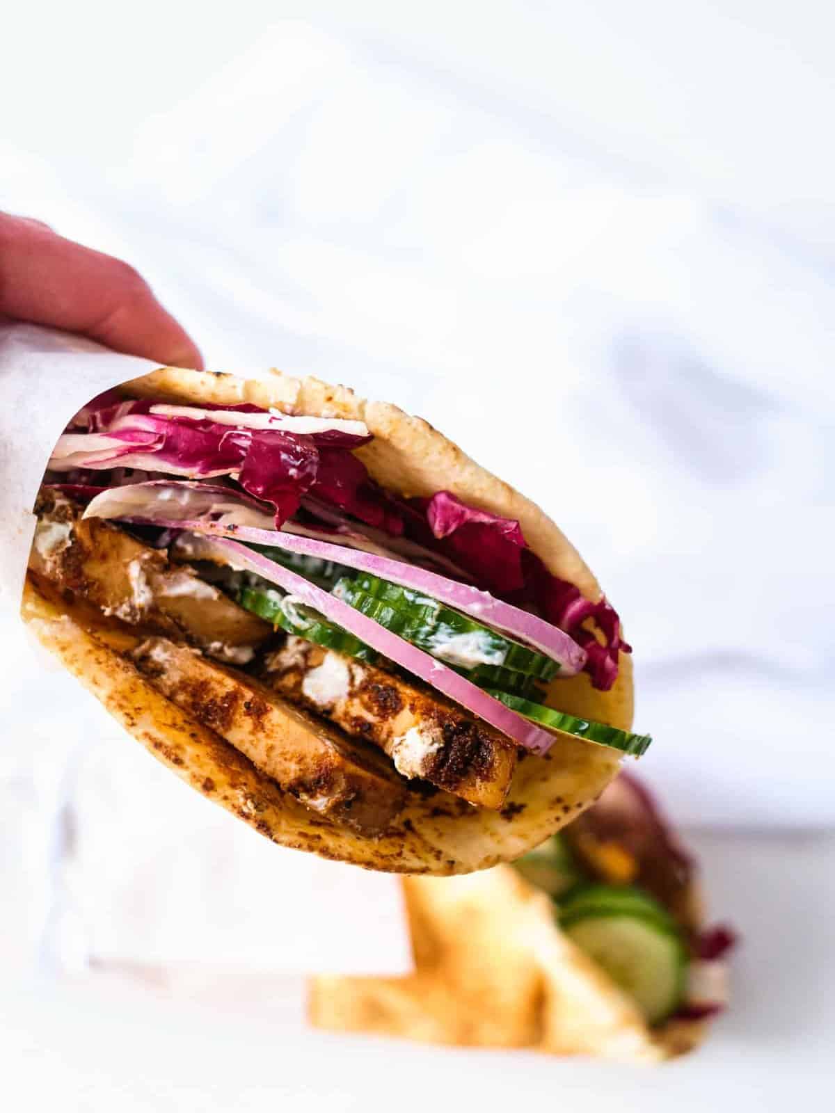 A person is holding a chicken shawarma wrap with red onion and cucumber. 