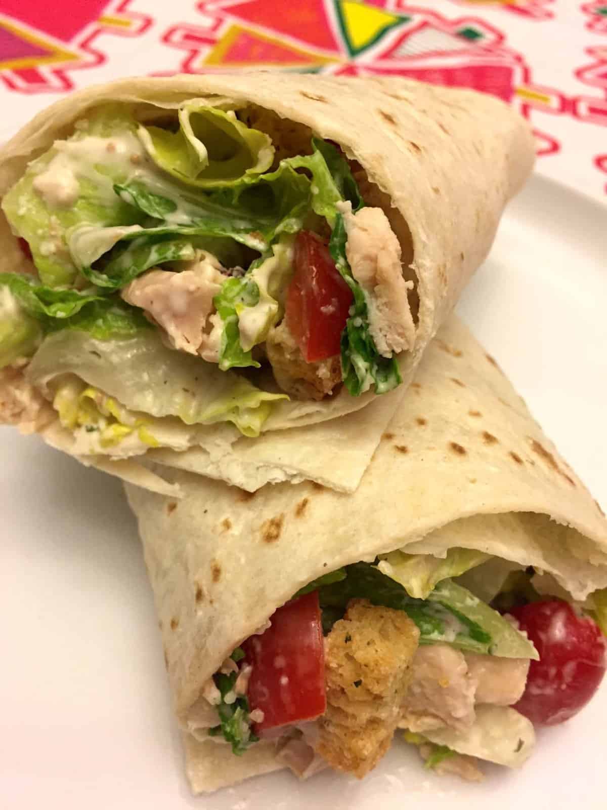 Two chicken Caesar wraps with lettuce, croutons, and tomatoes on a plate.