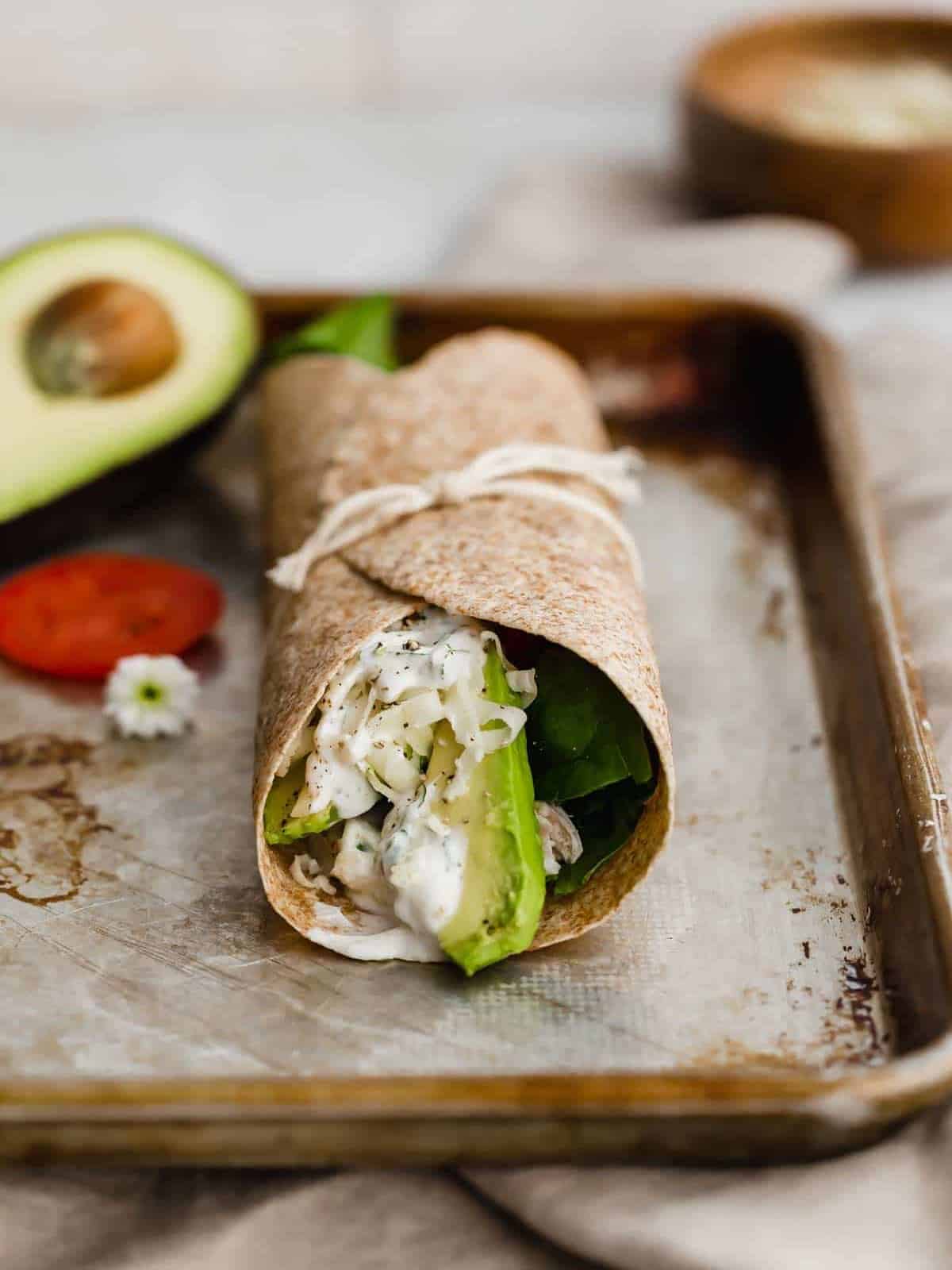 A healthy chicken wrap with avocado and tomatoes on a tray.