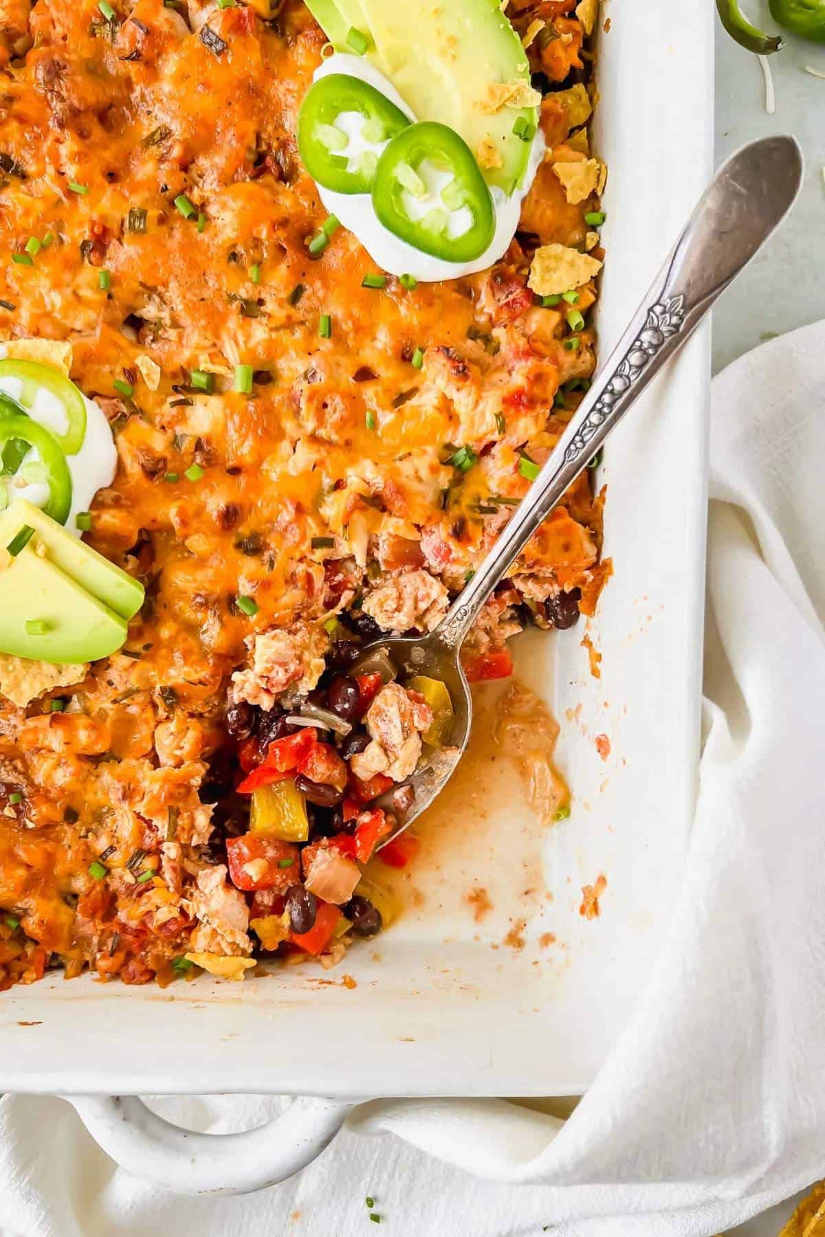 A macro friendly chicken taco casserole dish with a spoon in it. Topped with avocado and sour cream. 