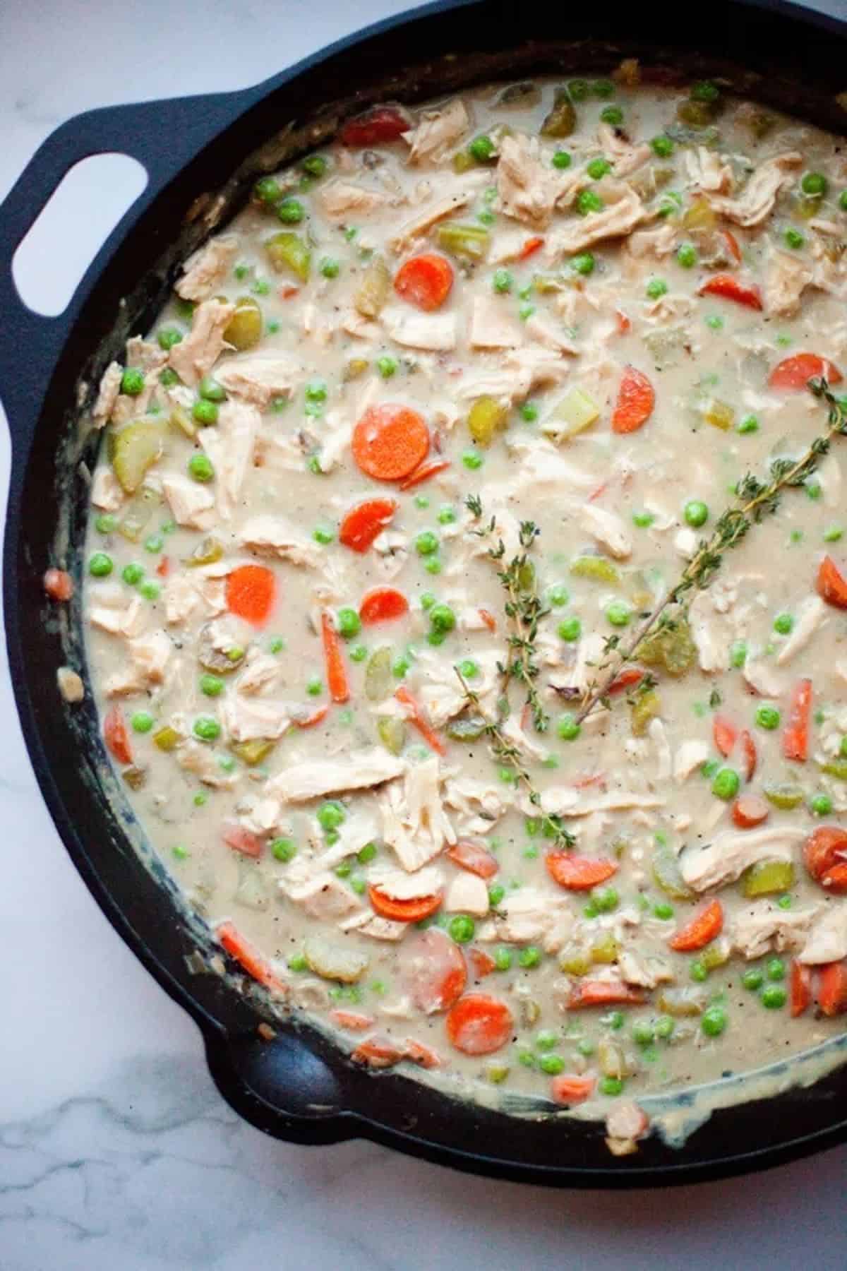 Chicken pot pie soup with carrots and peas in a large pot. 