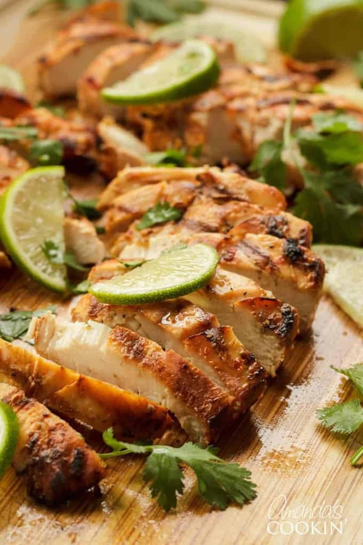 Grilled chicken on a cutting board with lime wedges.