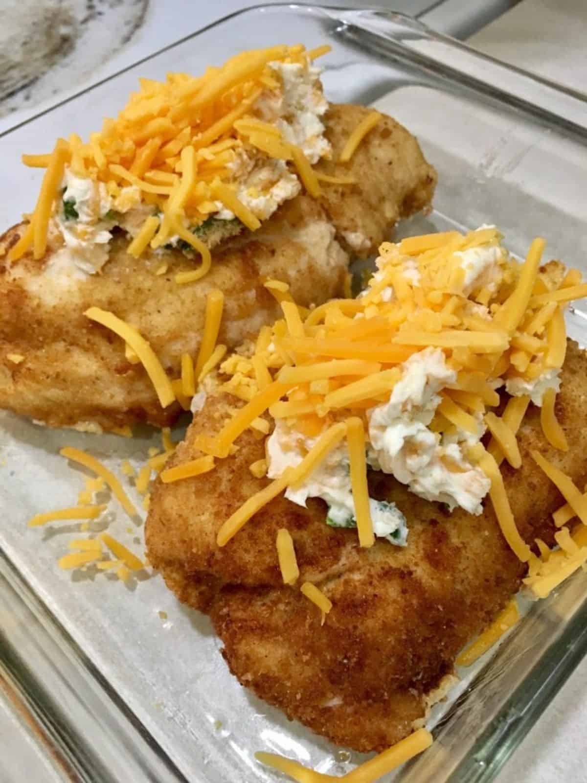Two jalapeno popper chicken breasts topped with melty cheese and a cream cheese in a baking dish.